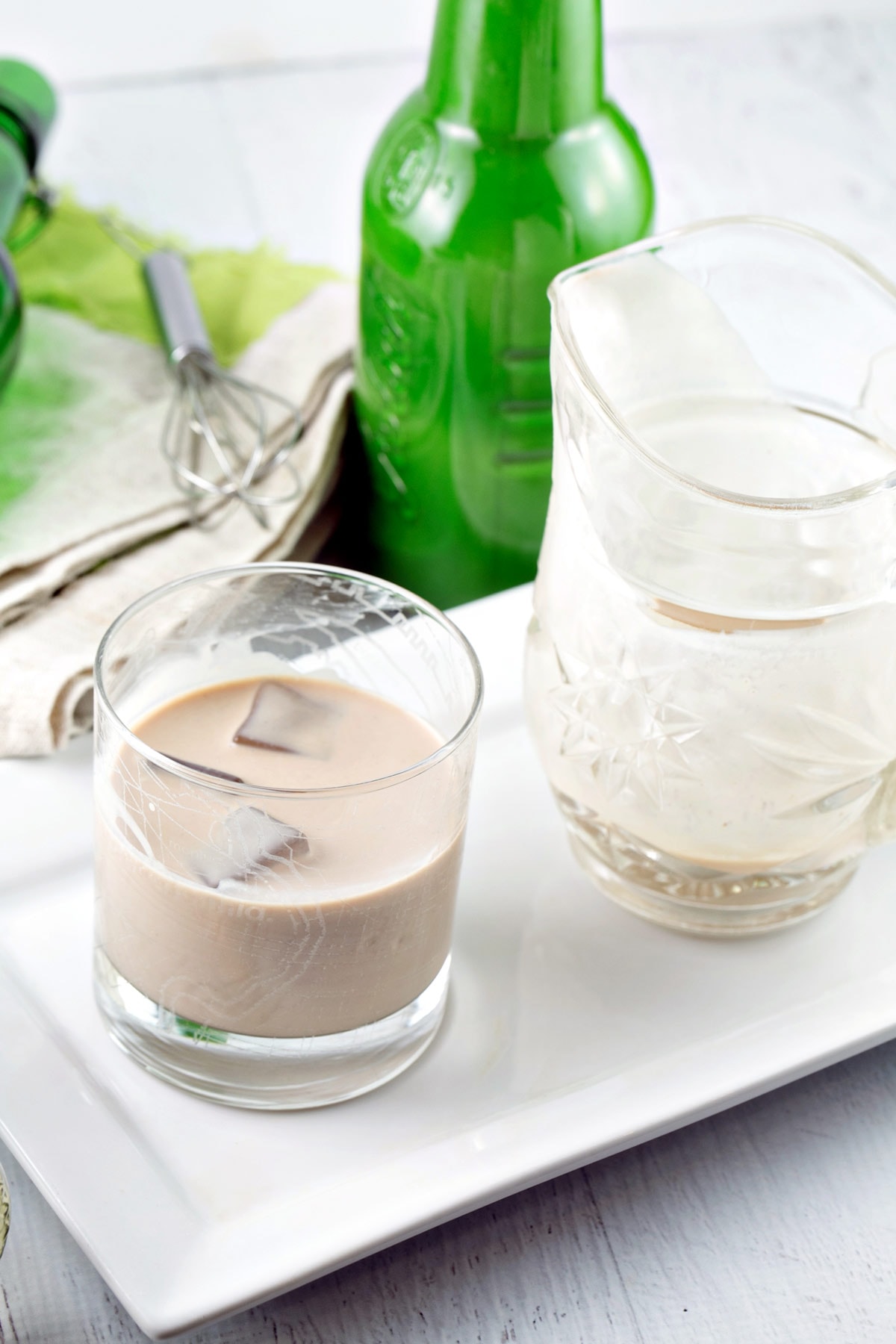 rocks glass filled with irish cream next to a small pitcher and green swing top bottle.