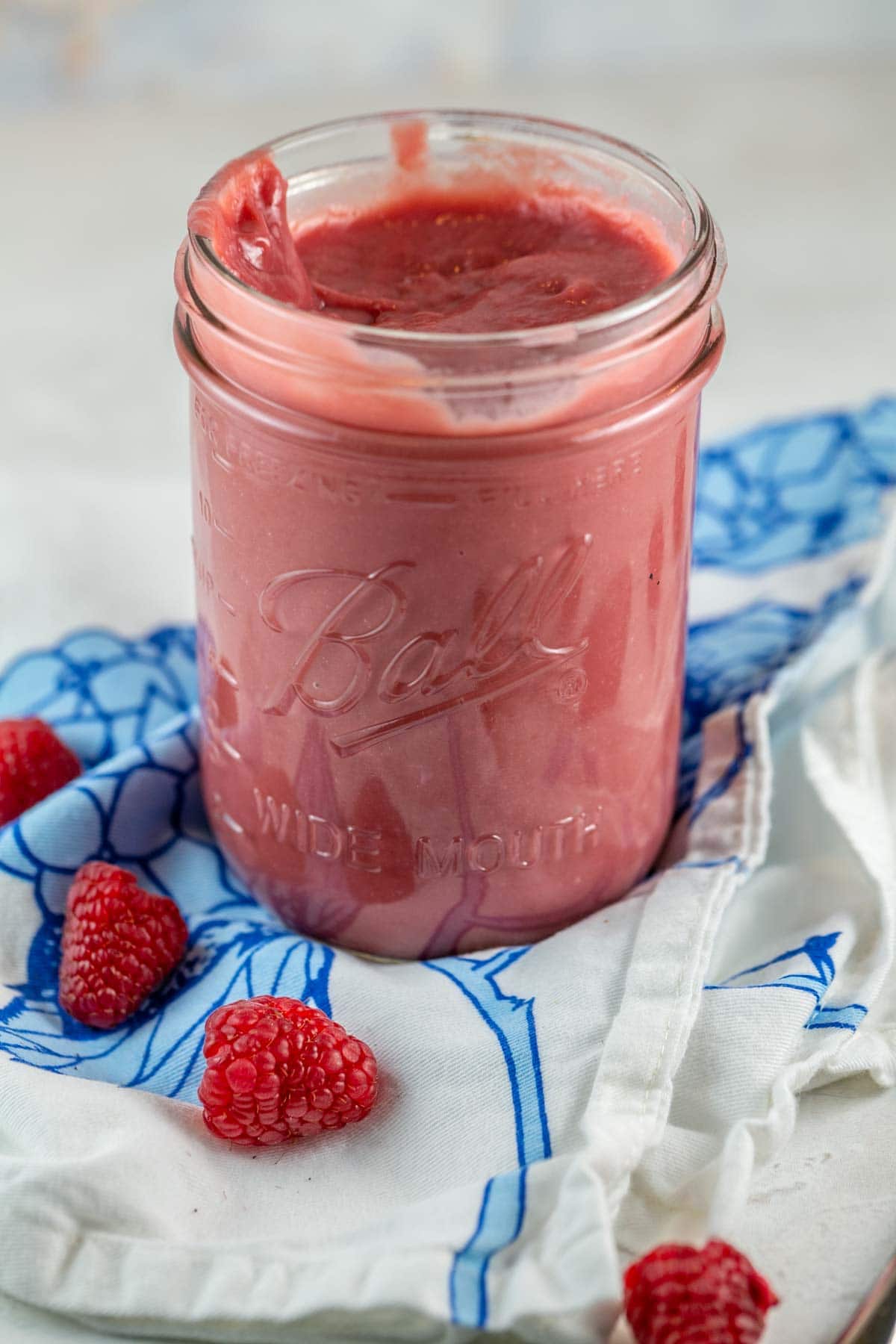 pink raspberry curd in a glass mason jar surrounded by fresh raspberries