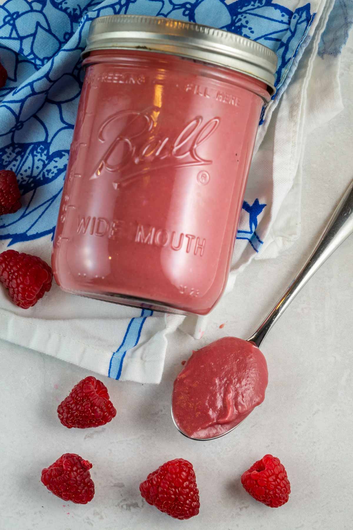 jar of raspberry curd lying on its side surrounded by fresh raspberries