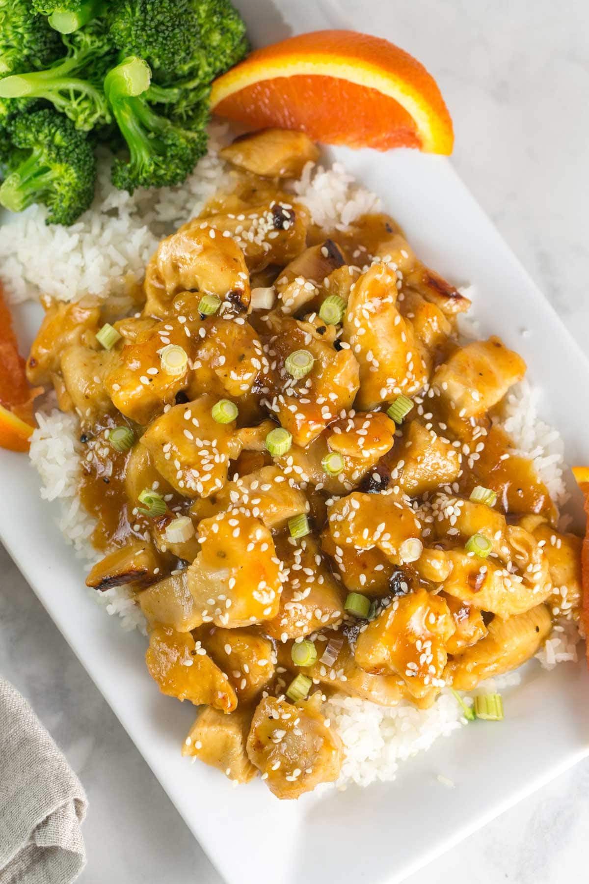 homemade orange chicken sprinkled with sesame seeds and scallions on top of a pile of rice