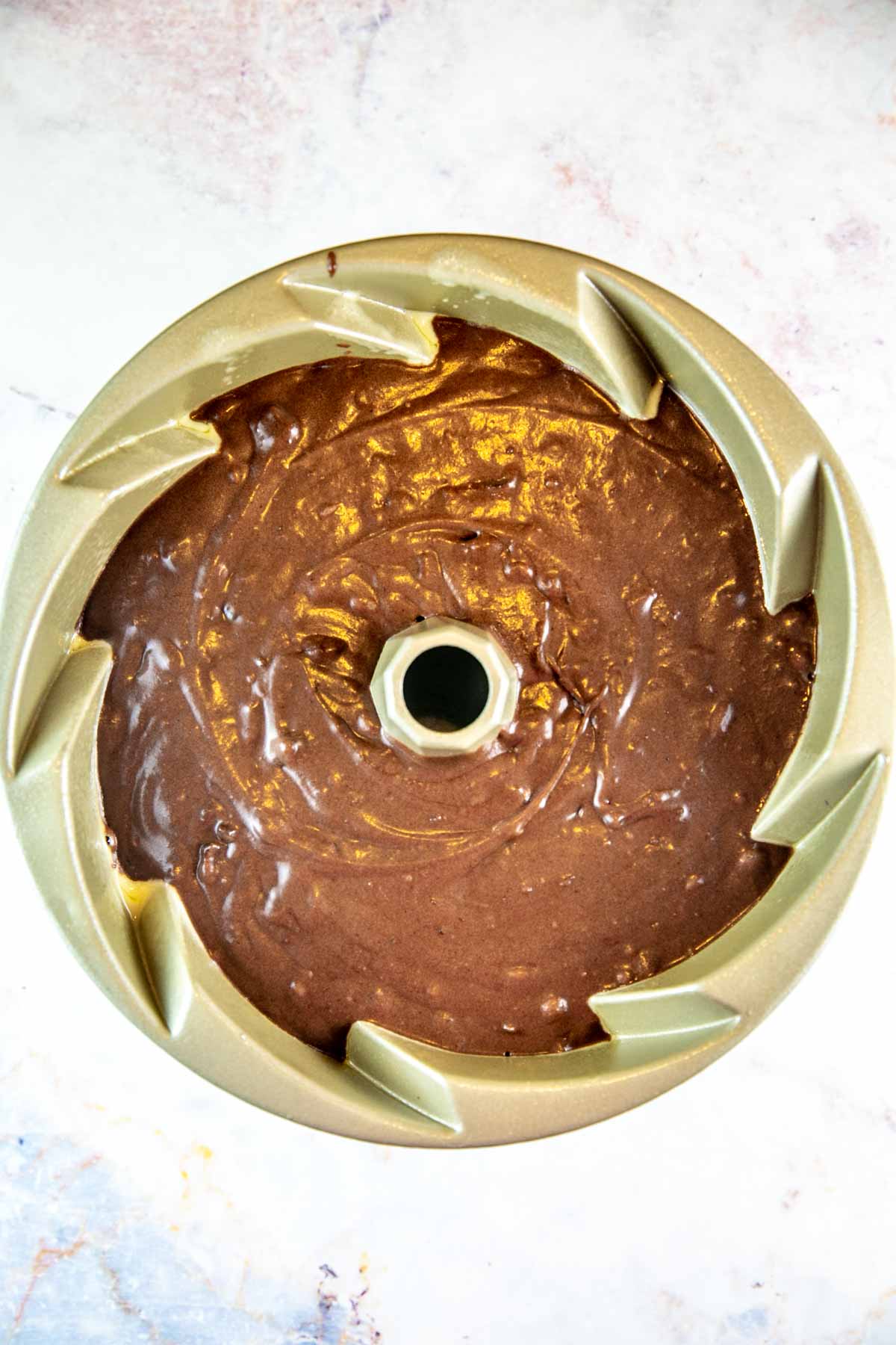 Chocolate cake batter in a gold bundt cake pan. 
