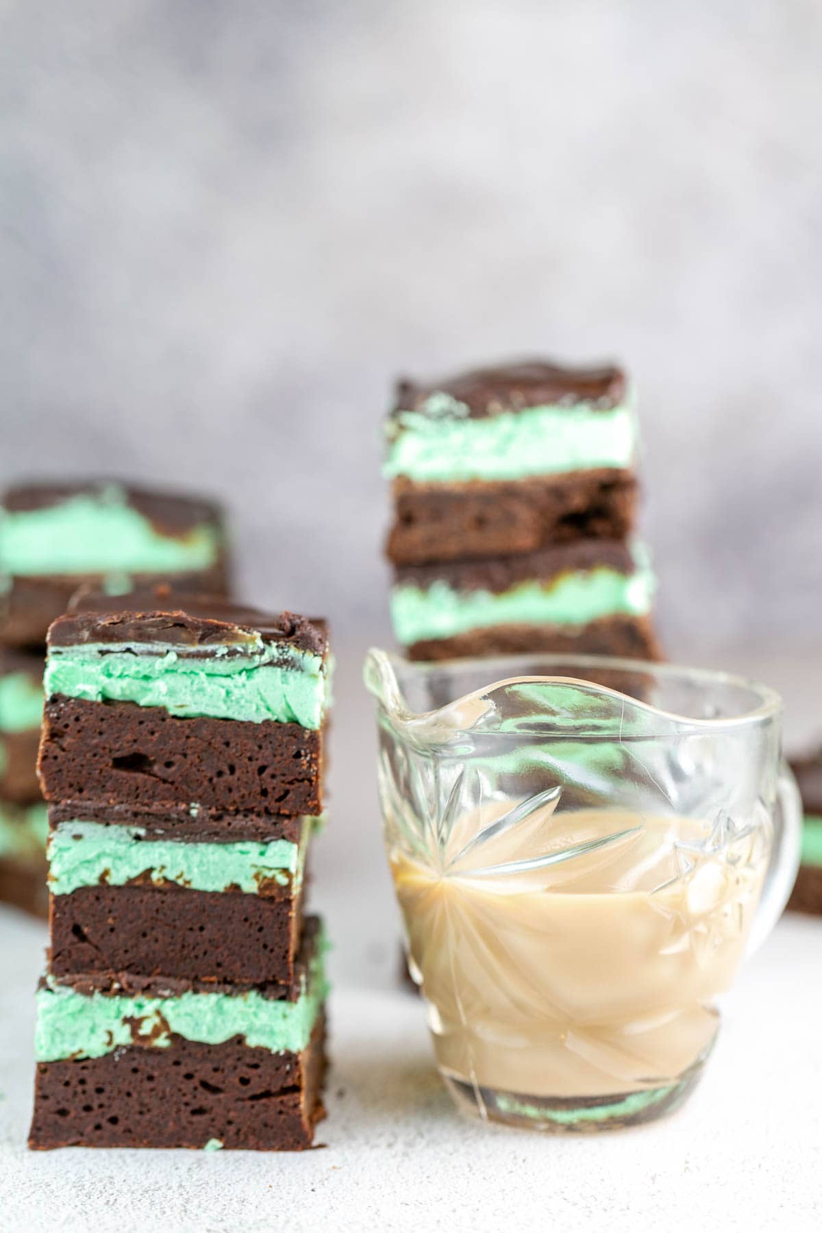 a stack of mint irish cream brownies next to a small pitcher of homemade irish cream