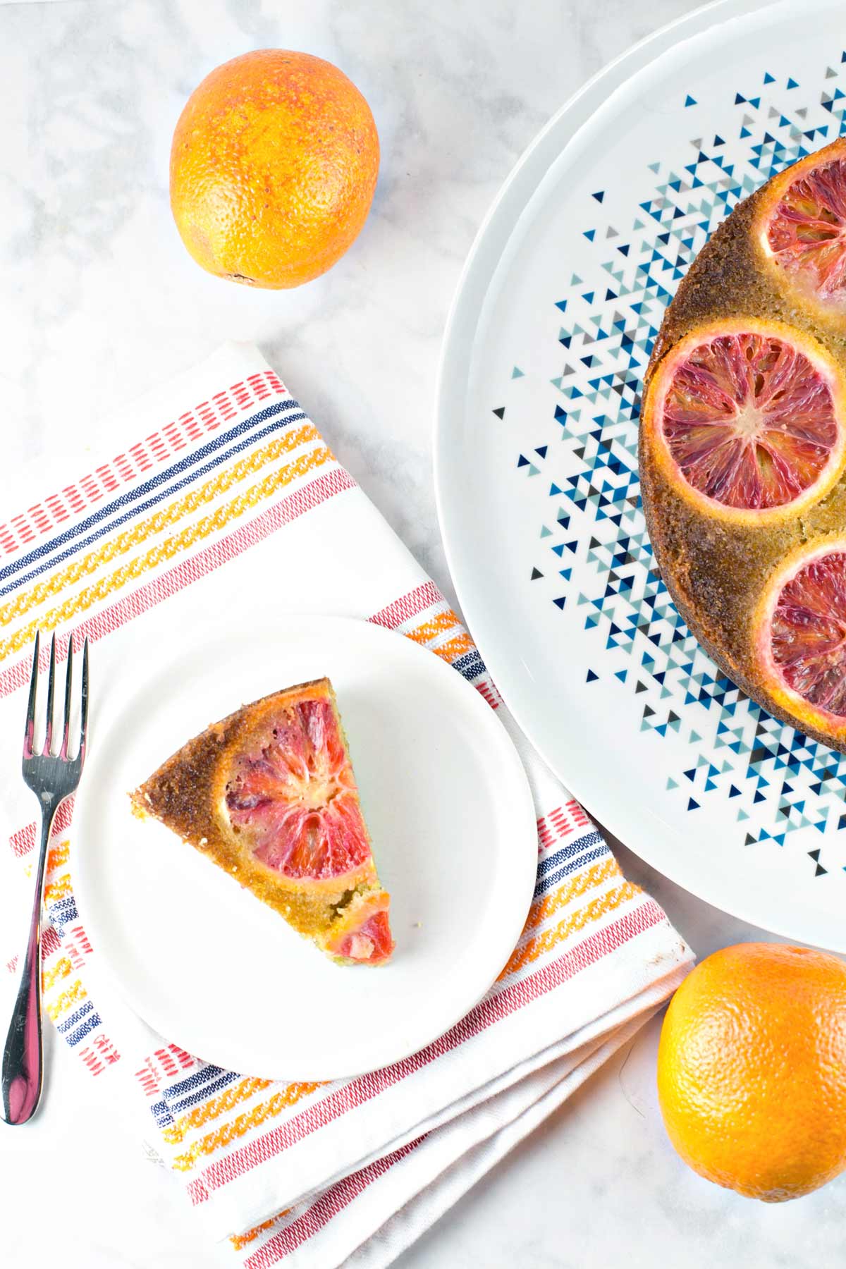 slice of olive oil cake topped with blood oranges next to the rest of the cake