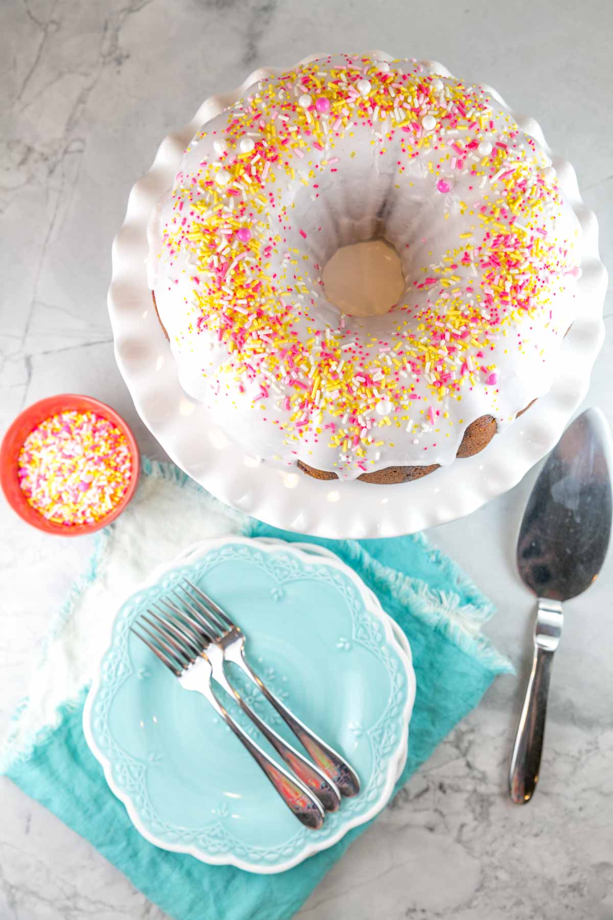 a lemon bundt cake with strawberry lemonade swirl covered in sprinkles on a white cake plate