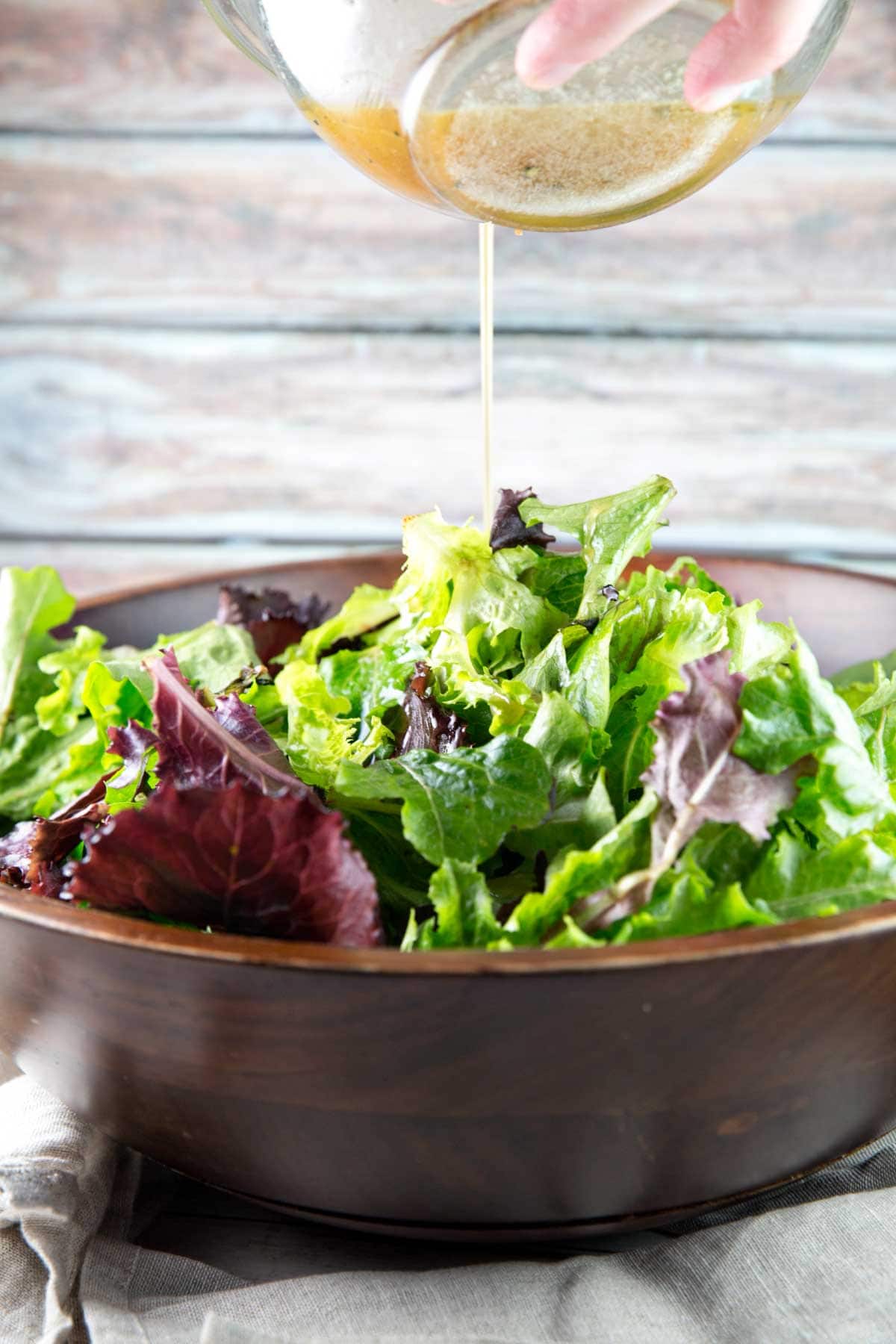 homemade salad dressing being poured onto a bowl of leafy greens 