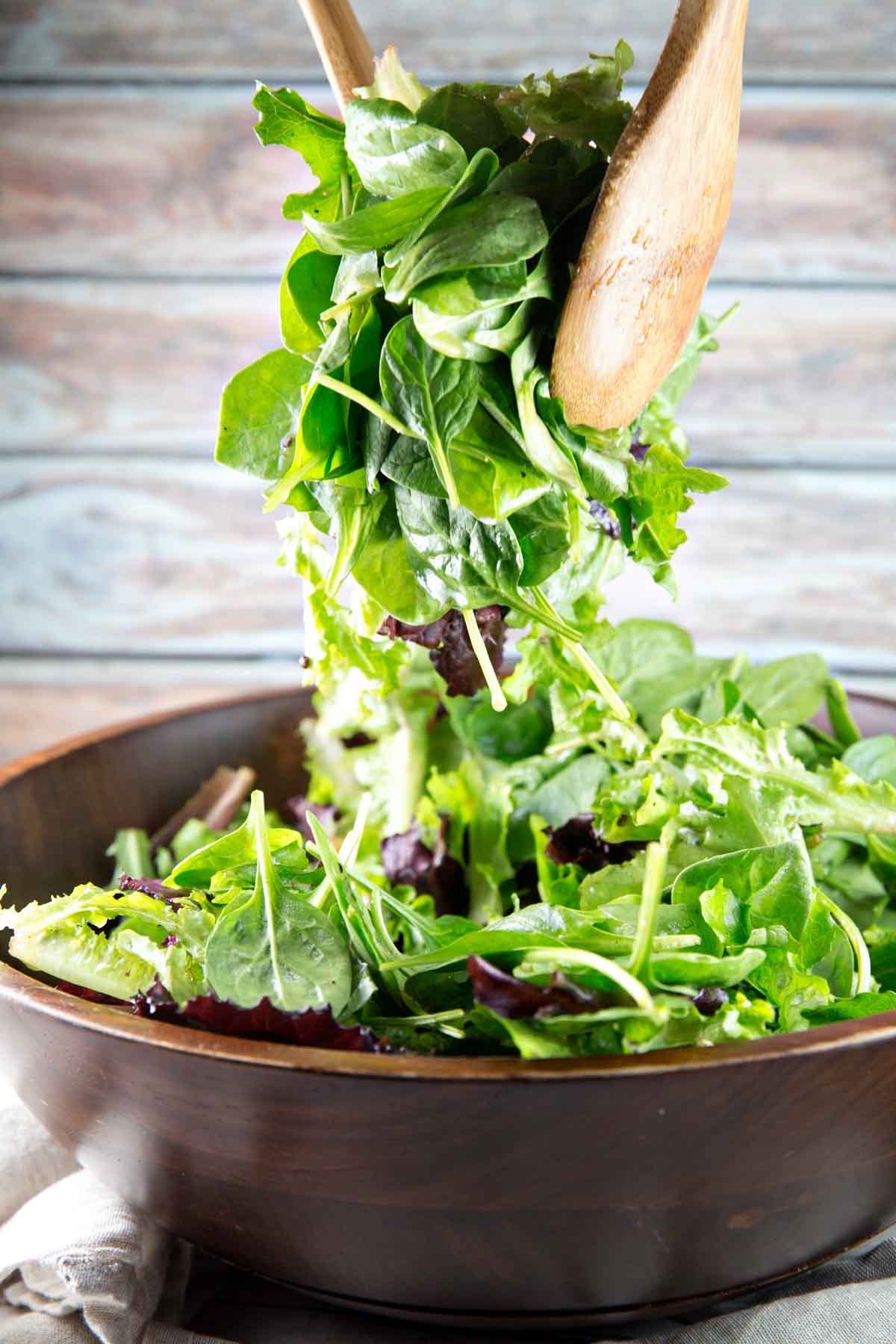 two wooden salad spoons tossing a big pile of greens for a roasted beet salad