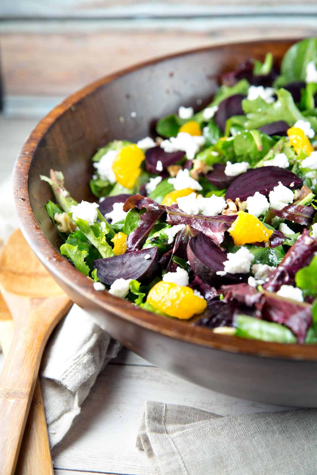a large wooden salad bowl filled with a roasted beet salad with mandarin oranges and goat cheese