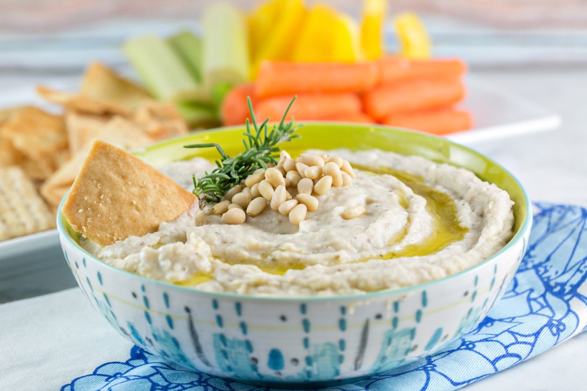 bowl filled with white bean dip with pine nuts and a drizzle of olive oil