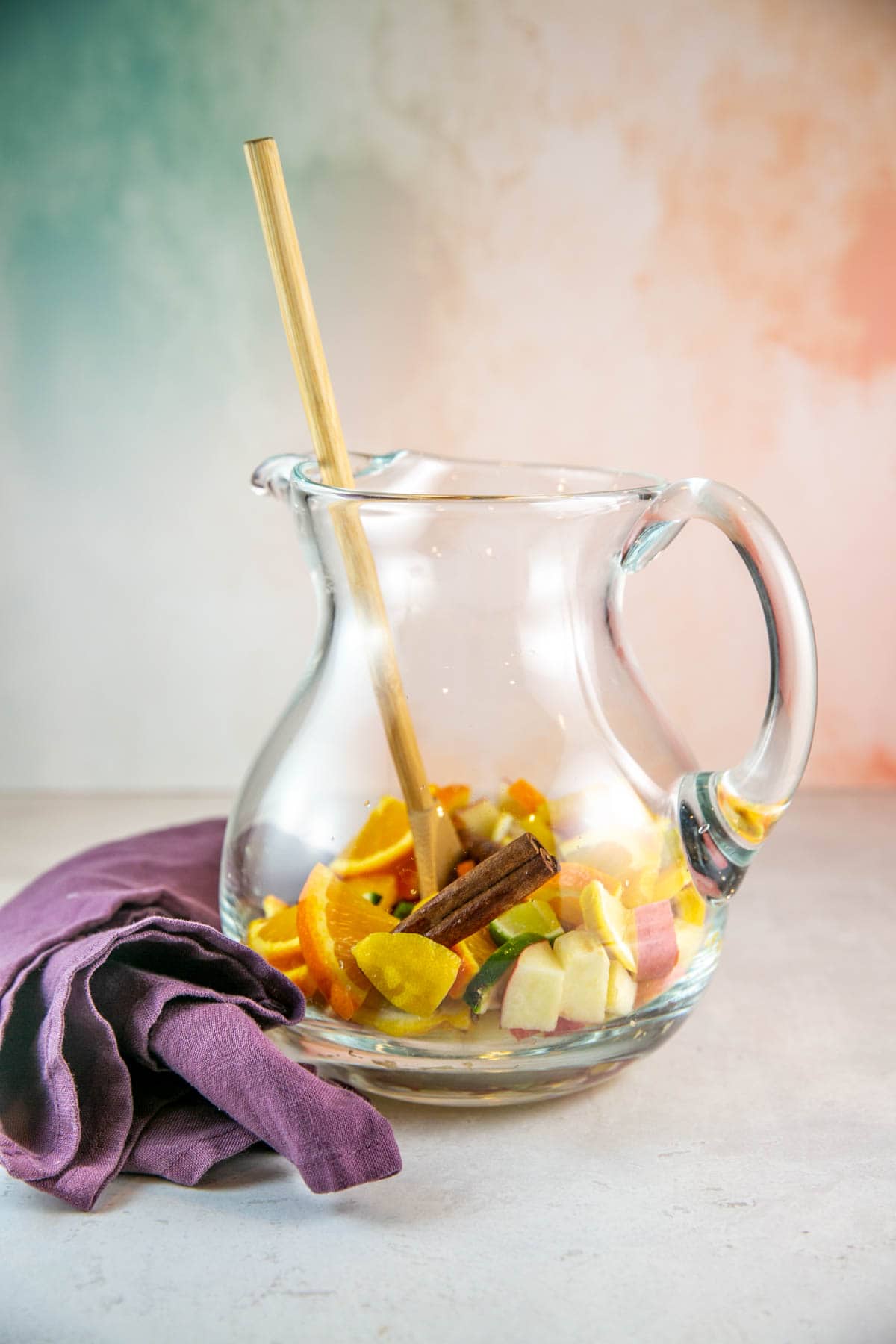 glass pitcher filled with chopped fruit and cinnamon sticks