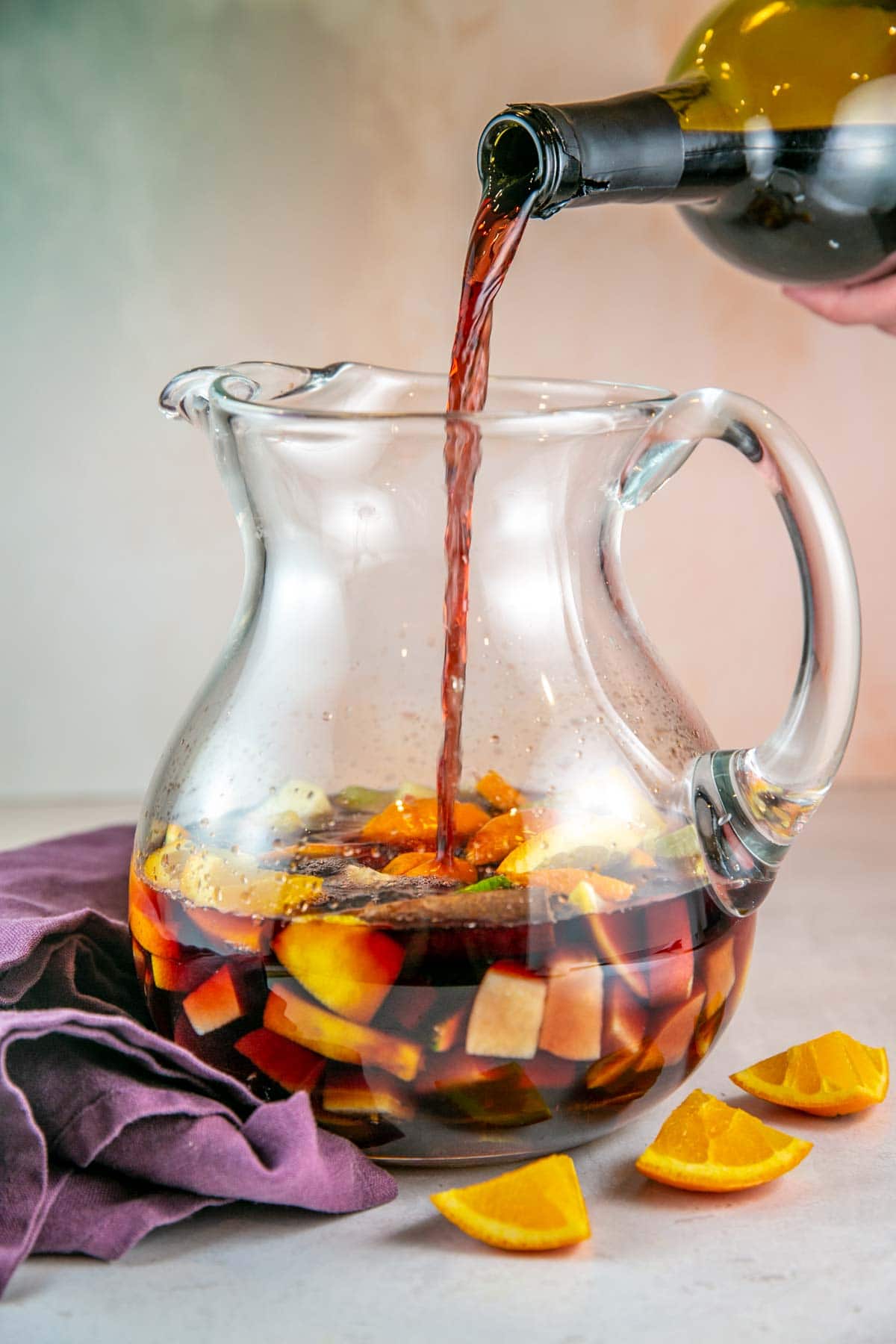 wine pouring out of the bottle into a pitcher filled with fruit