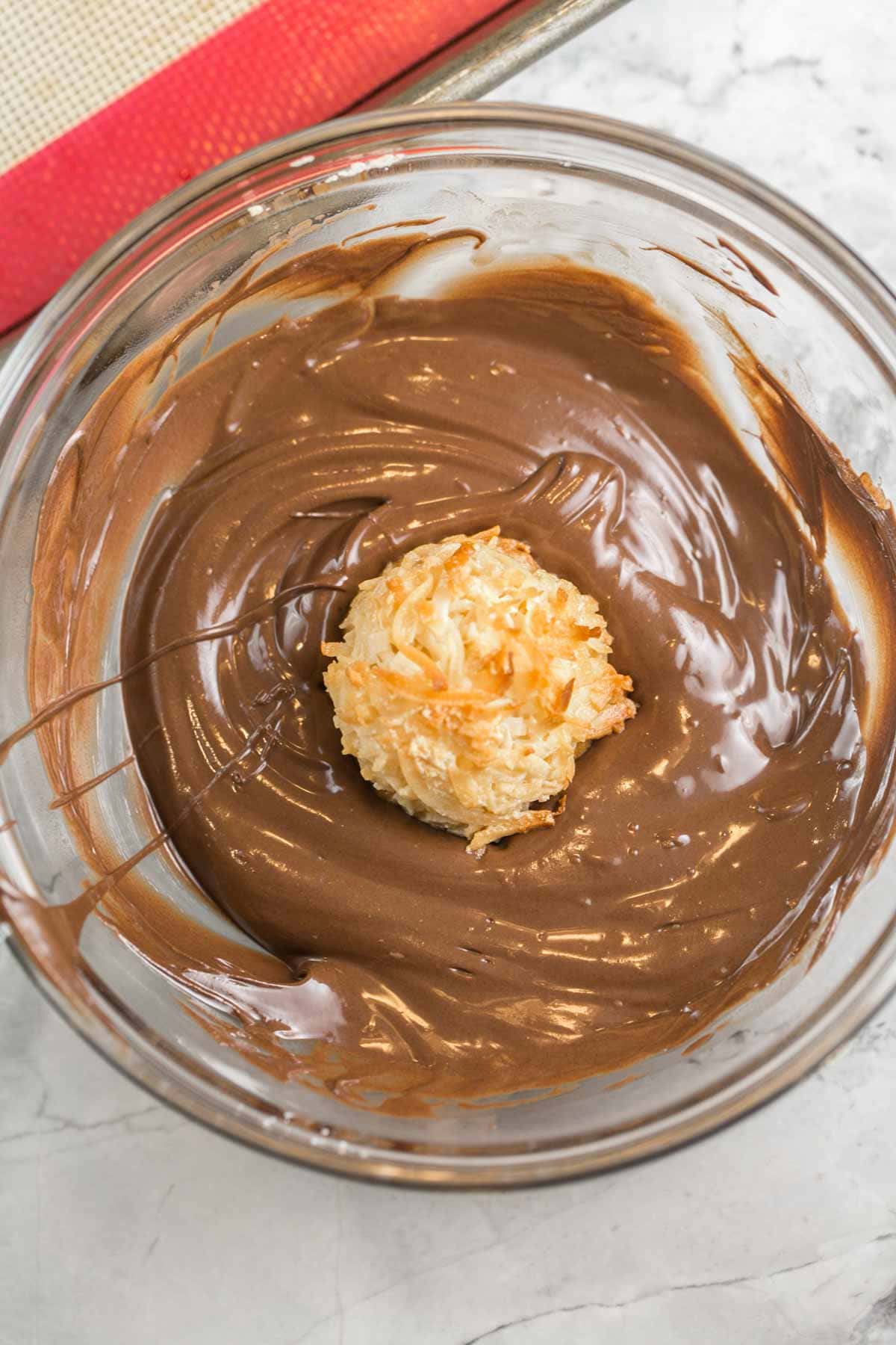 a lightly toasted coconut macaroon sitting in a bowl of melted chocolate