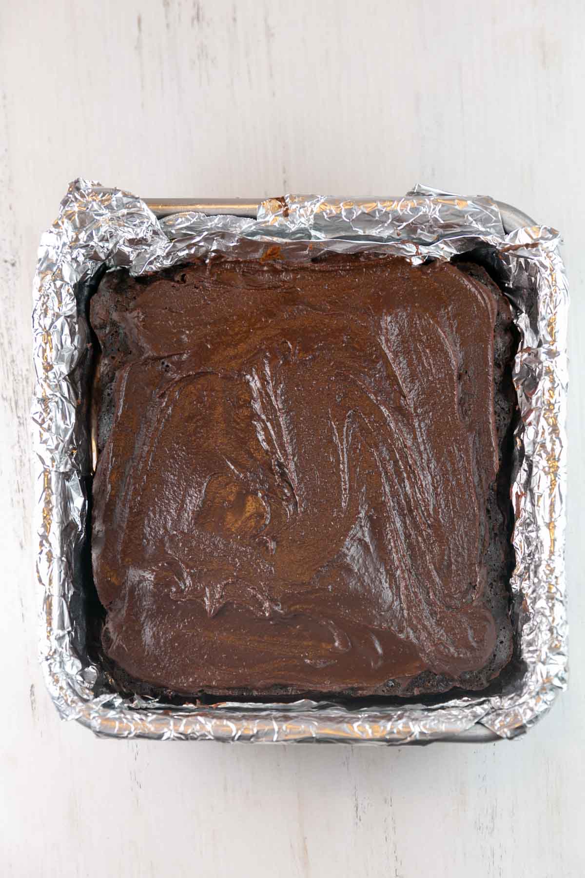 brownies in a baking pan covered with a layer of shiny chocolate frosting