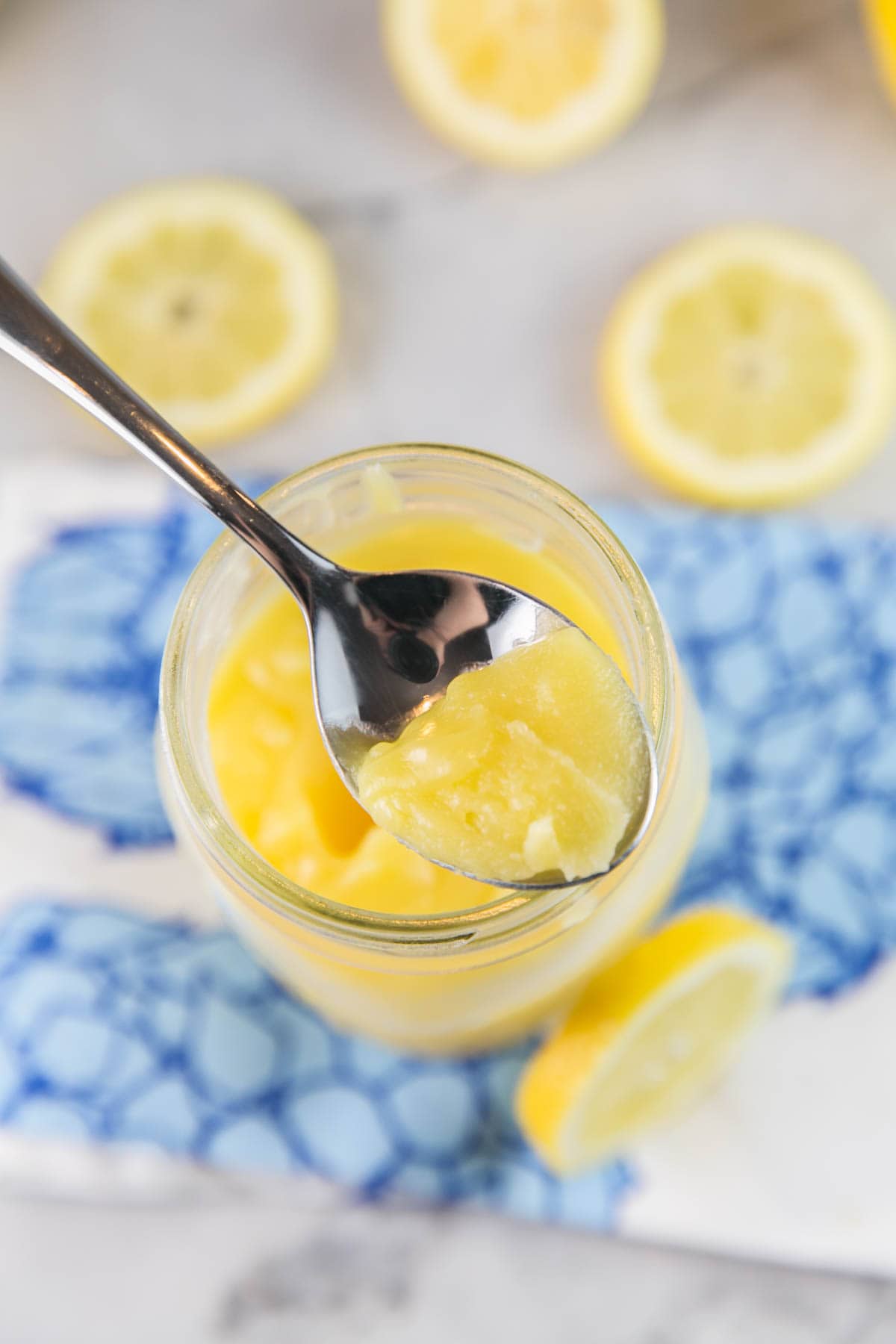 a spoon dipping into a jar of bright yellow homemade lemon curd