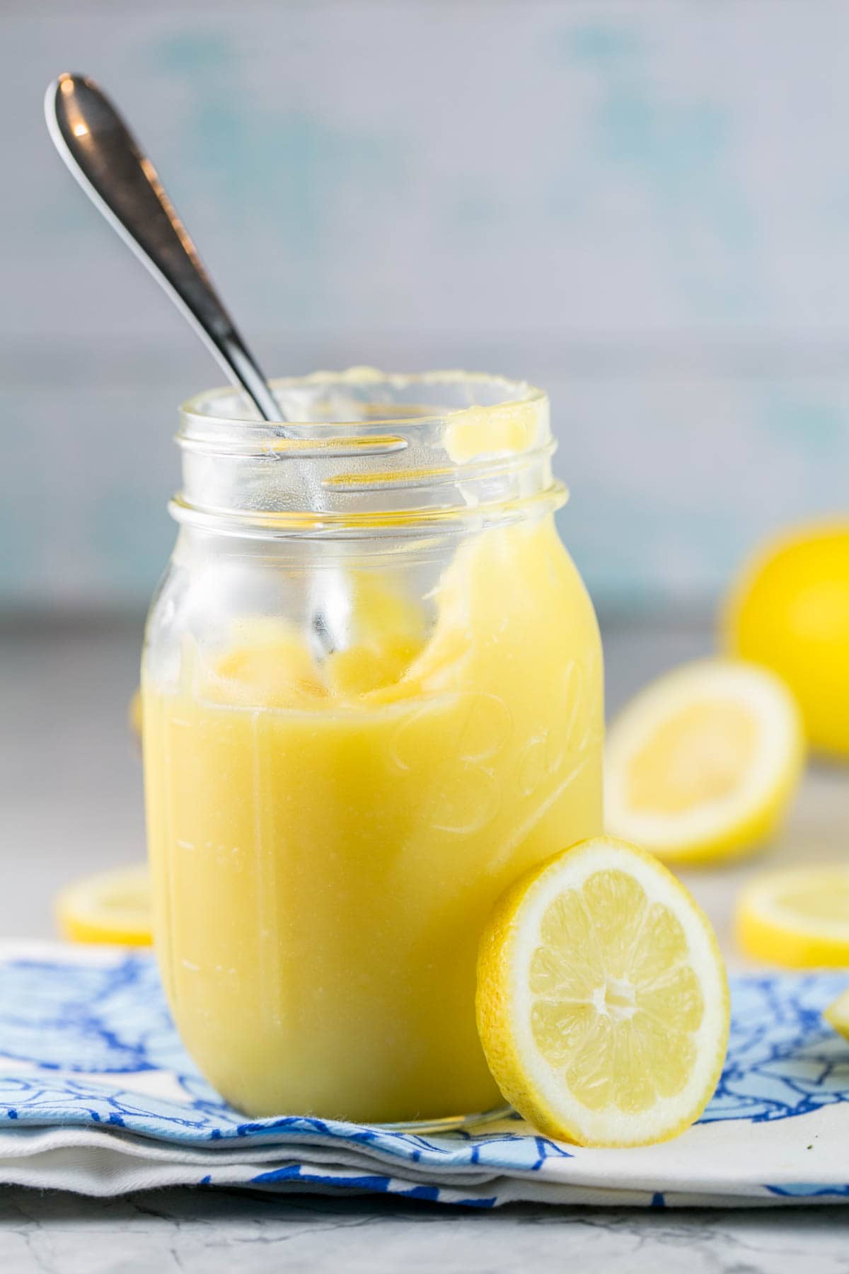 a glass mason jar filled with homemade lemon curd surrounded by sliced lemons