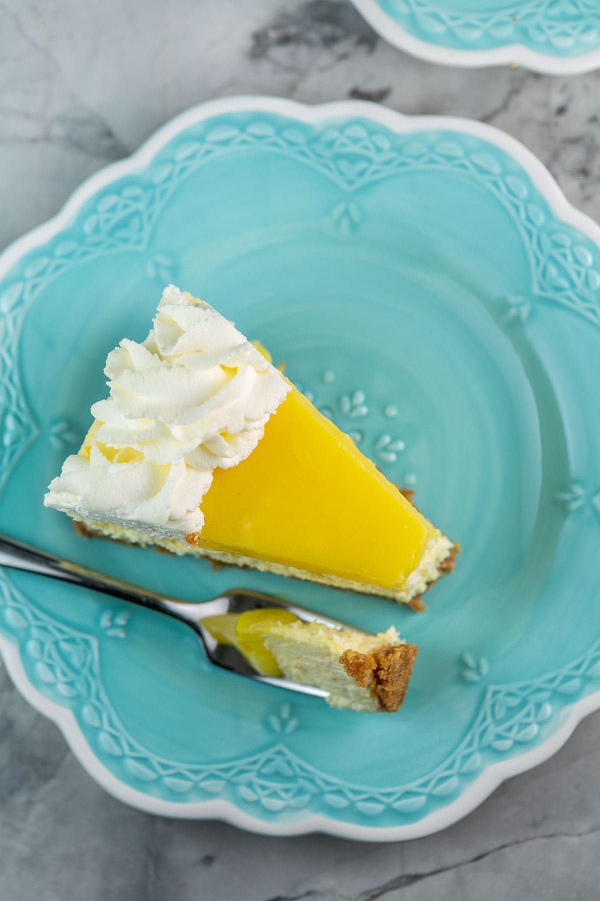 overhead view of a slice of cheesecake covered with lemon curd on a blue dessert plate