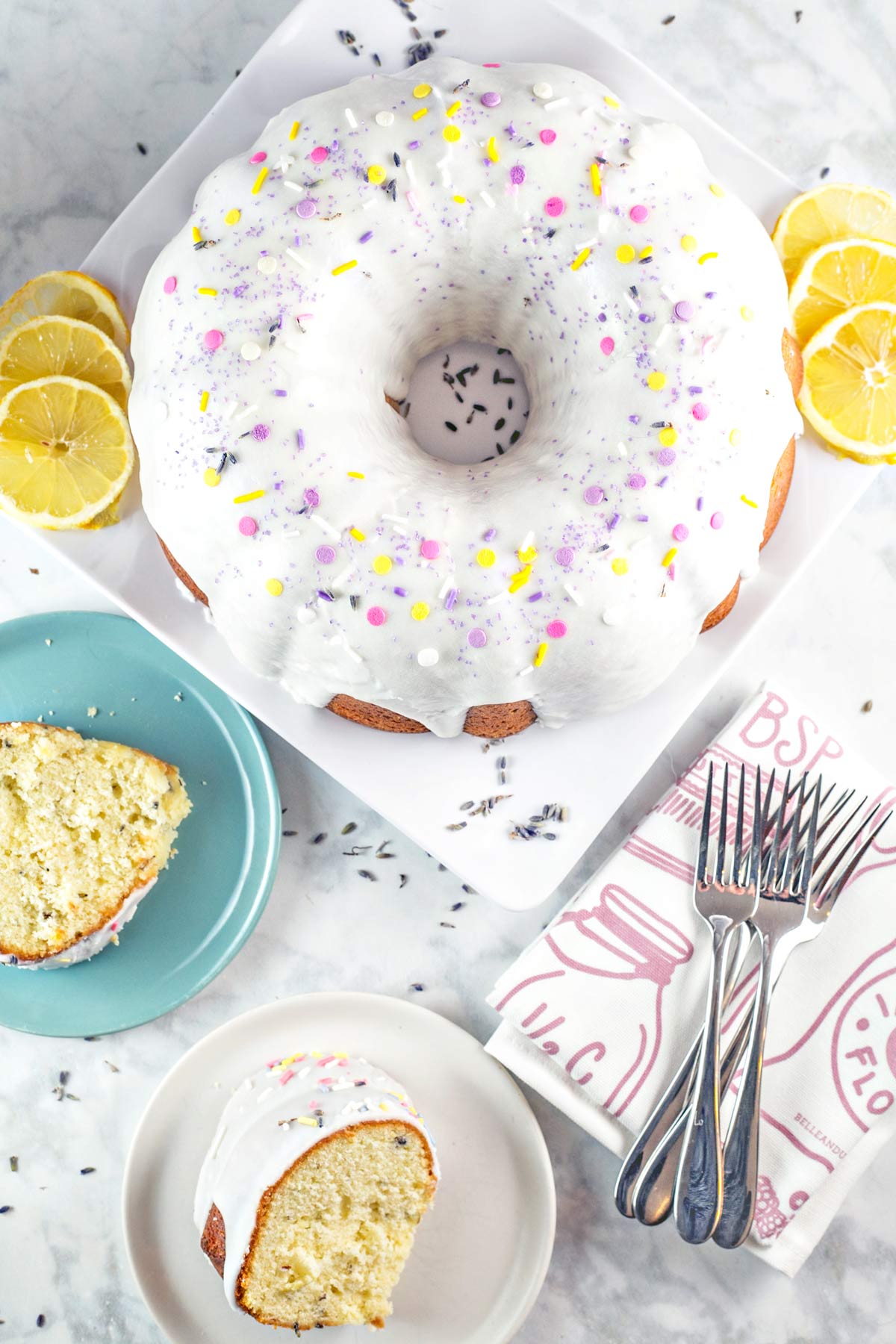 bundt cake covered in vanilla glaze surrounded by sliced lemons and lavender buds