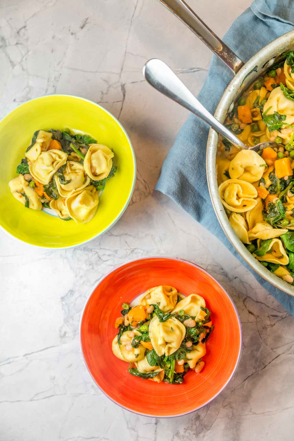 a skillet of tortellini with sweet potatoes and sausage dished into two brightly covered bowls
