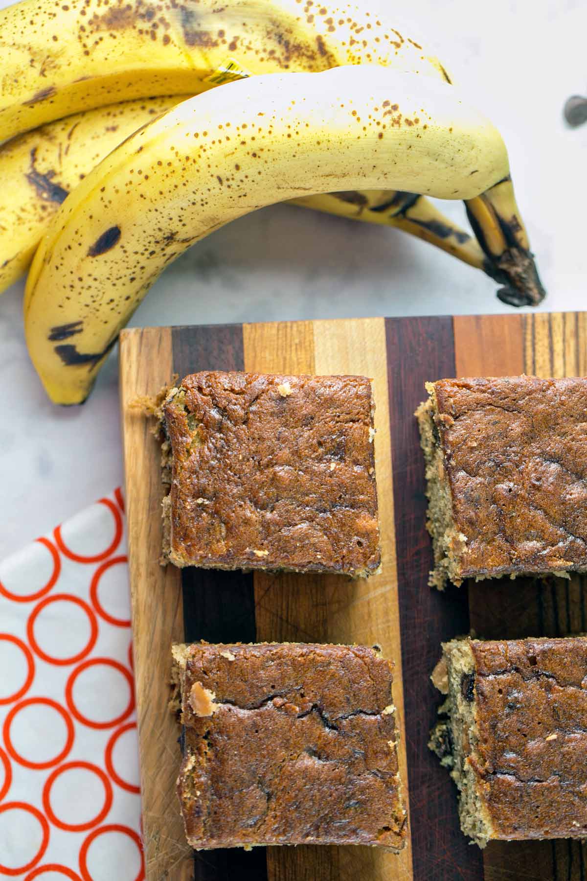 four banana cake bars next to spotted brown bananas