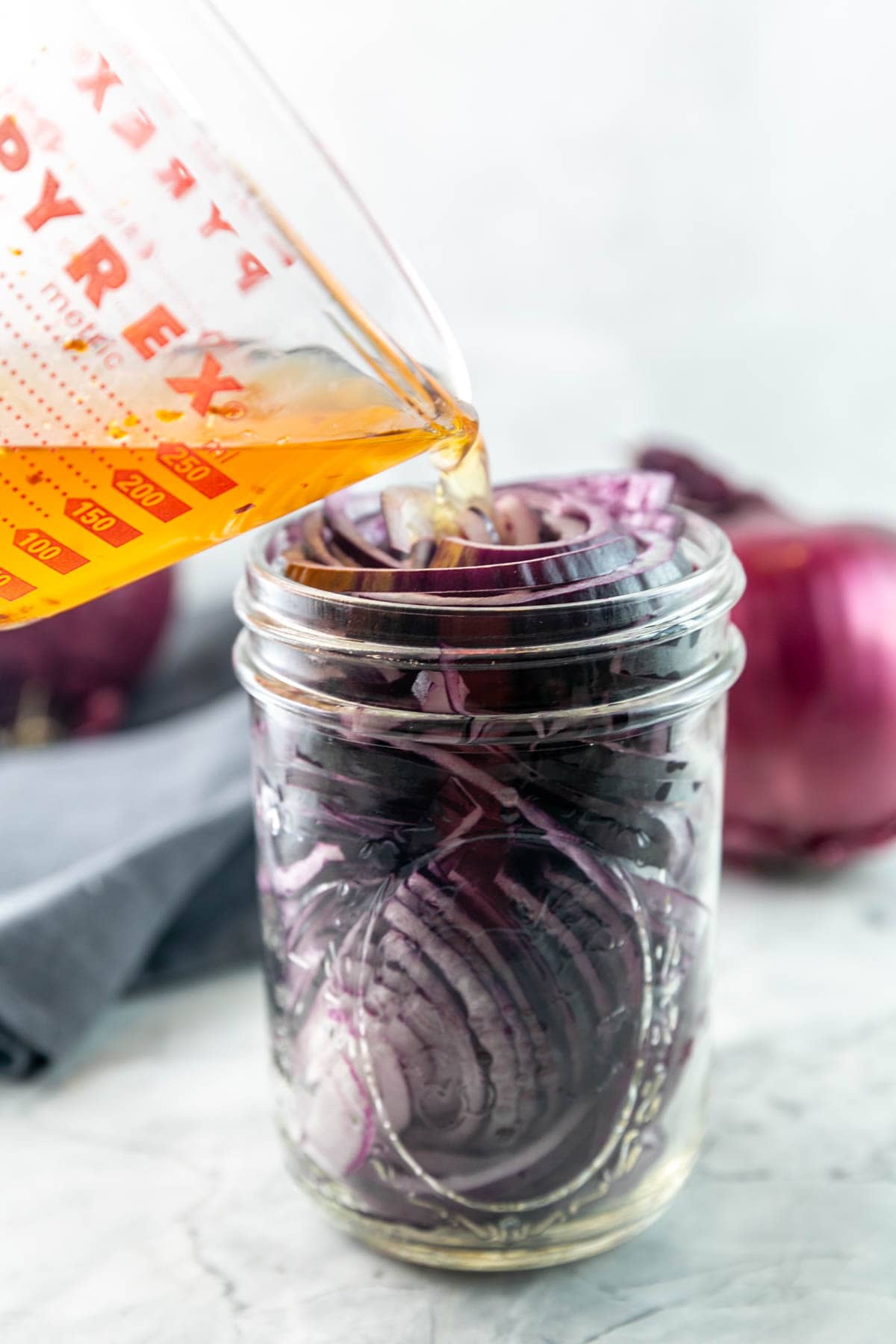 pouring the brining solution into a jar filled with thinly sliced red onions