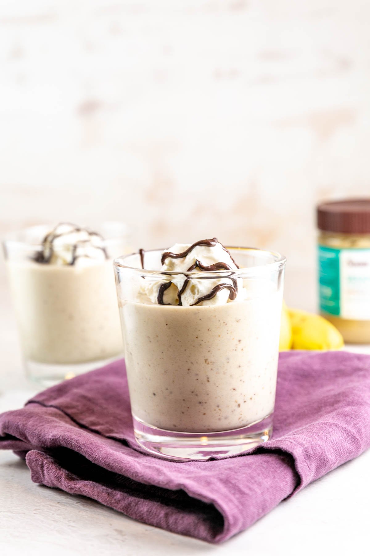 two glasses filled with homemade tahini shakes topped with whipped cream and a drizzle of chocolate halva spread