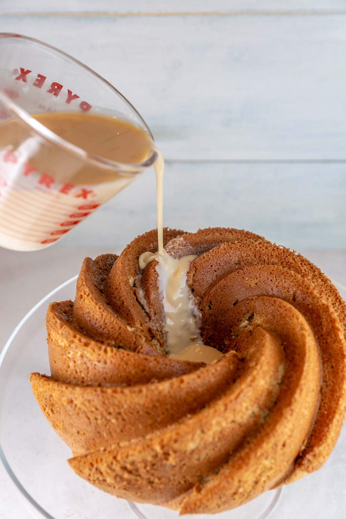 pouring a tres leches milk mixture from a measuring cup onto a bundt cake
