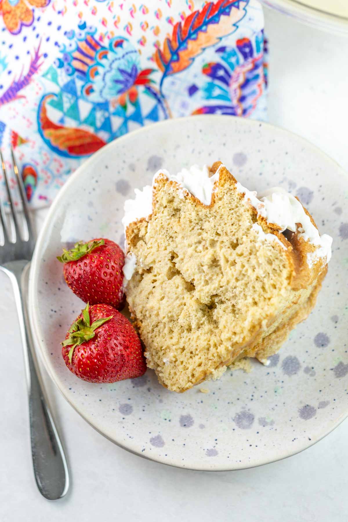 slice of cake on a speckled dessert plate with two strawberries