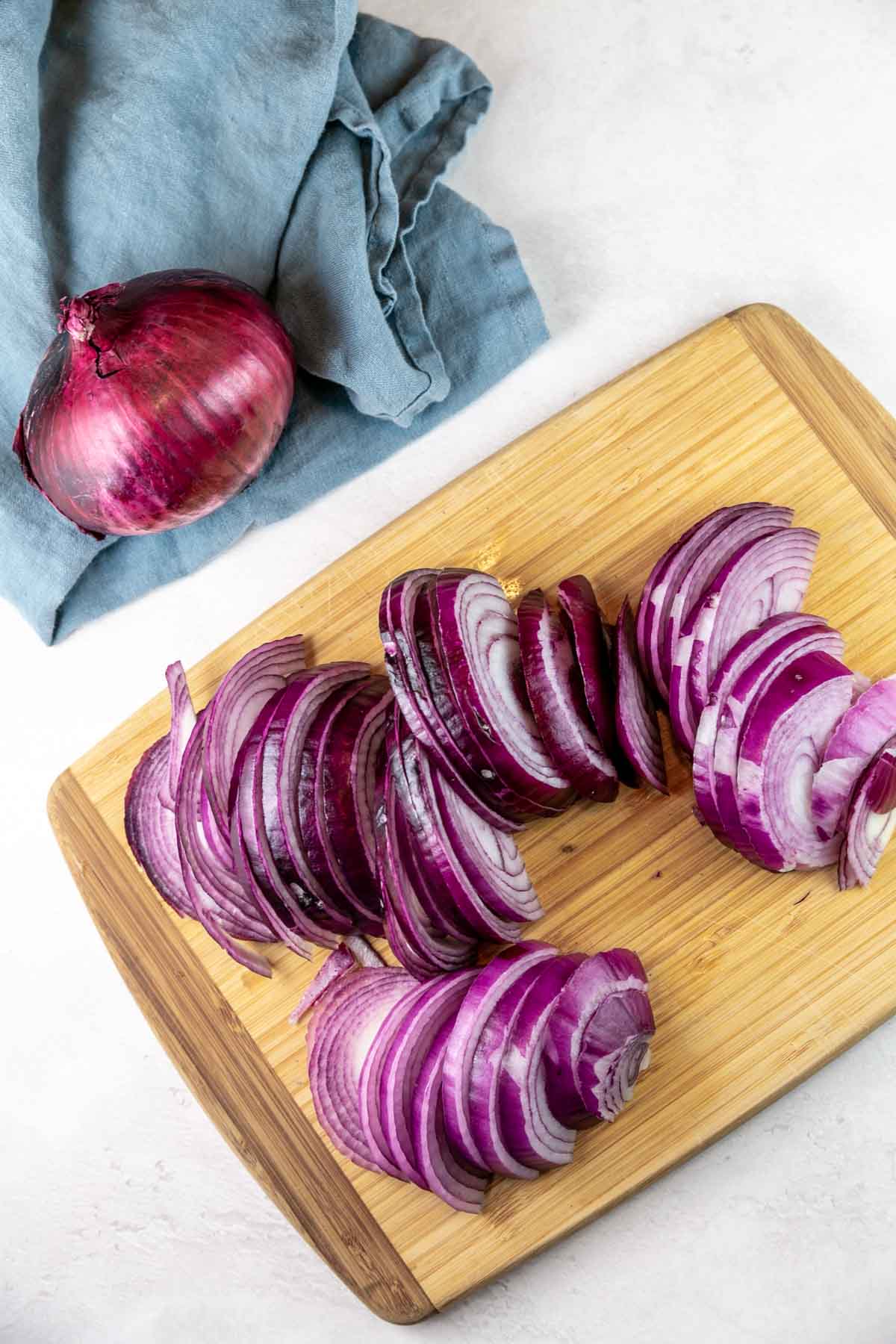 thiny sliced red onions on a wooden cutting board