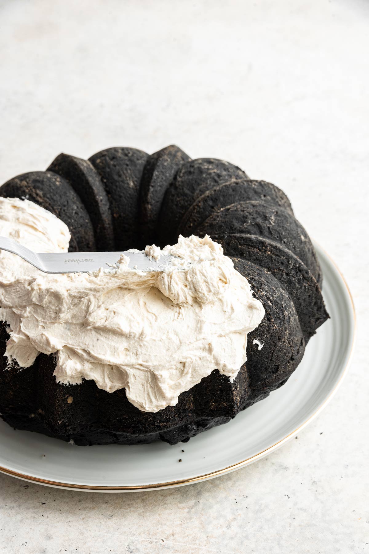 using an offset spatula to spread marshmallow buttercream on a chocolate bundt cake