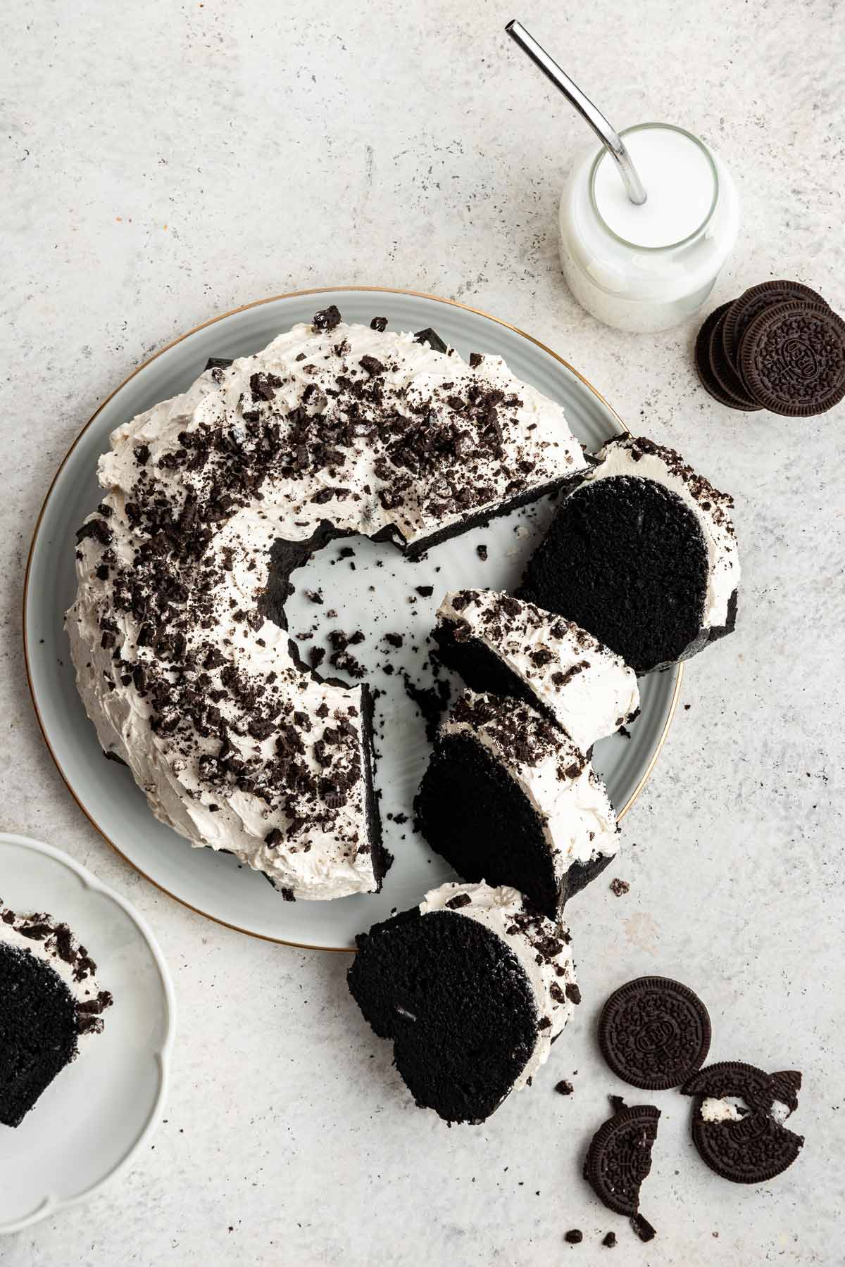 oreo bundt cake covered with marshmallow frosting on a cake plate with several slices of cake arranged on the plate