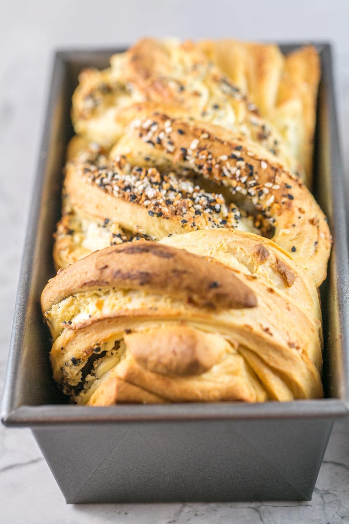 a loaf pan containing a freshly baked loaf of swirled everything bagel babka with a golden crust