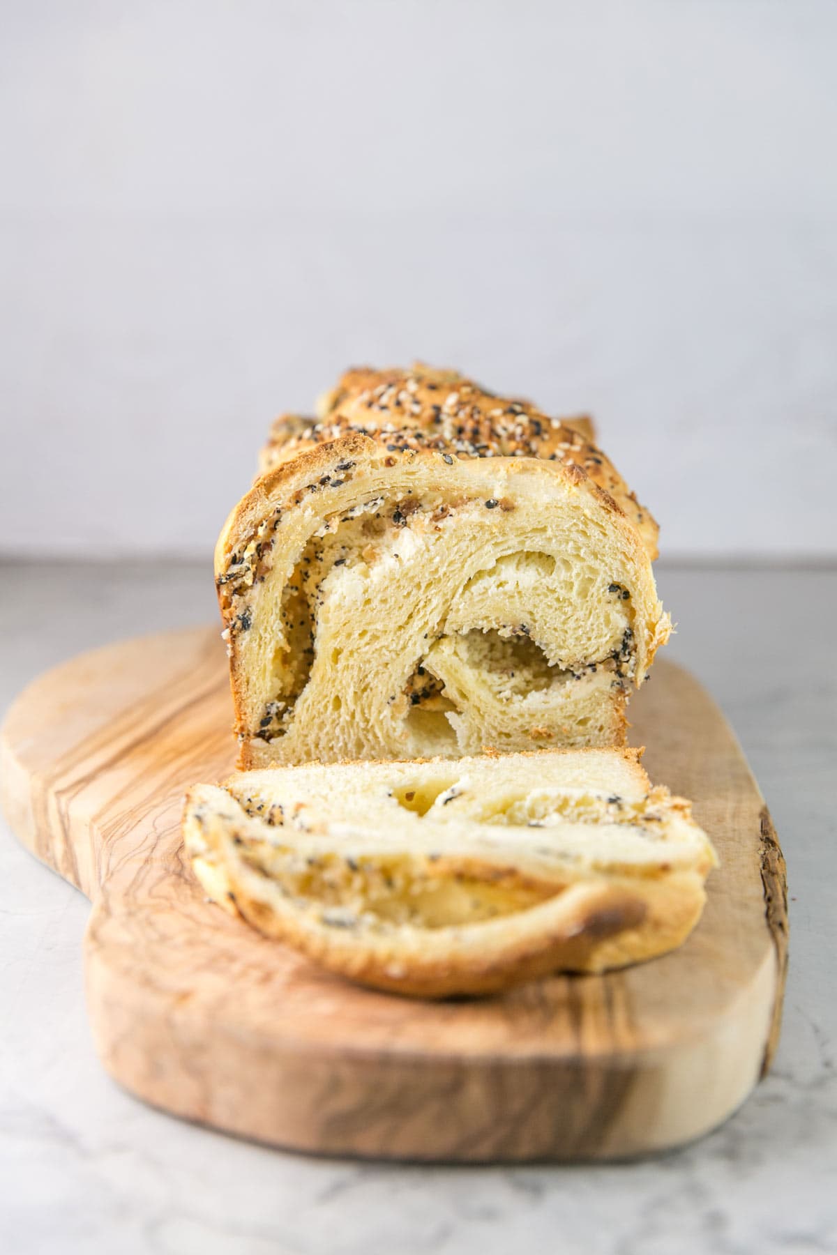 a loaf of everything bagel babka on a wooden board with one slice removed