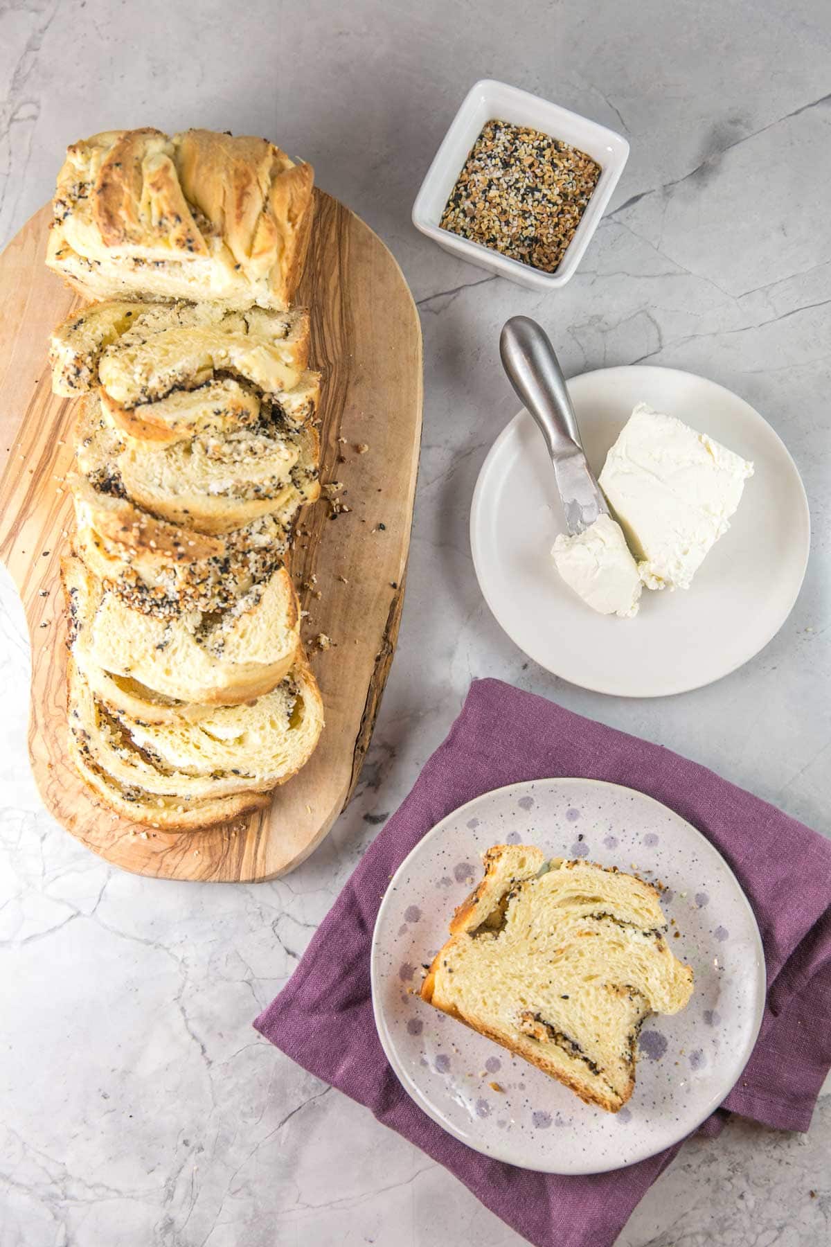 overhead view of the sliced babka with one piece on a small decorative plate next to a brick of cream cheese and everything bagel seasoning