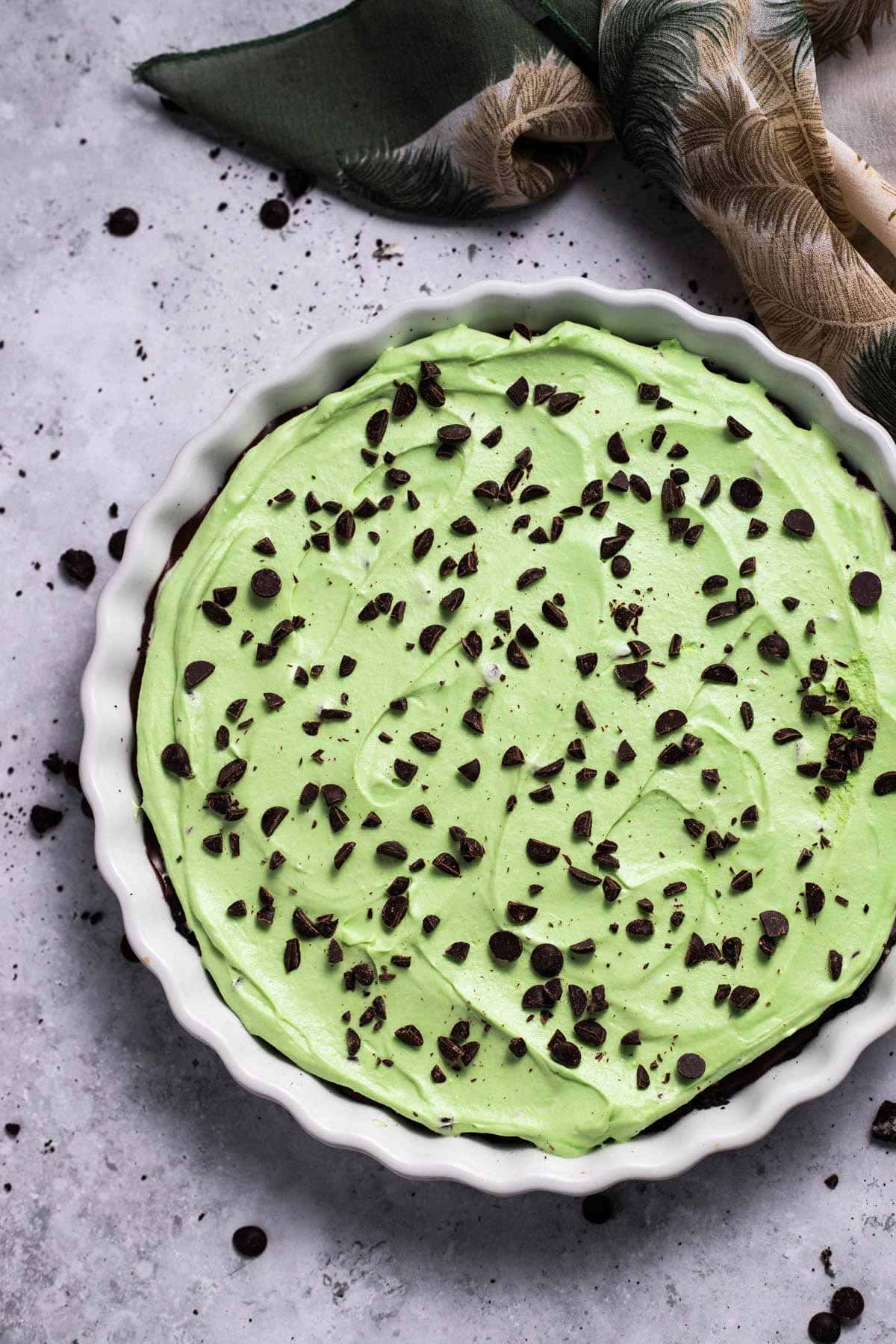 mint chocolate chip pie covered with chopped chocolate in a white pie plate