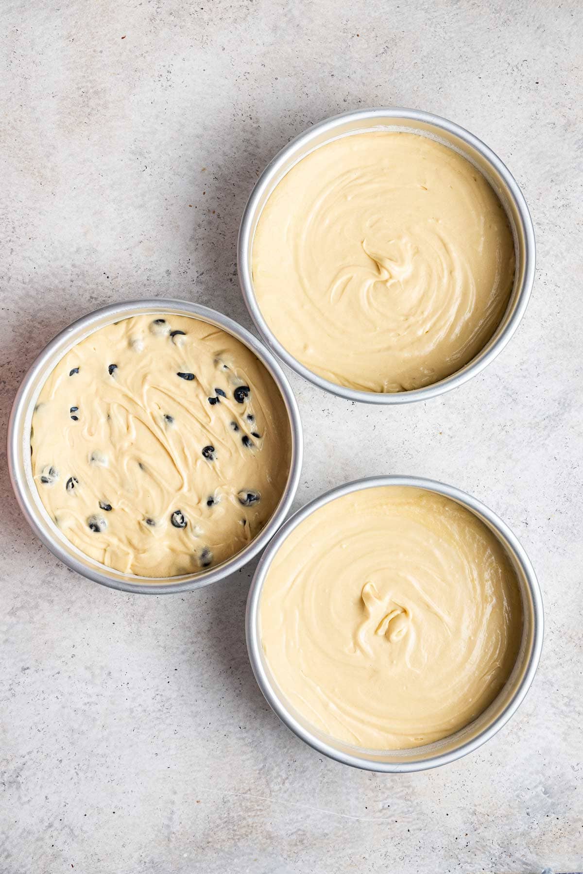 three cake pans filled with vanilla cake and blueberries before baking