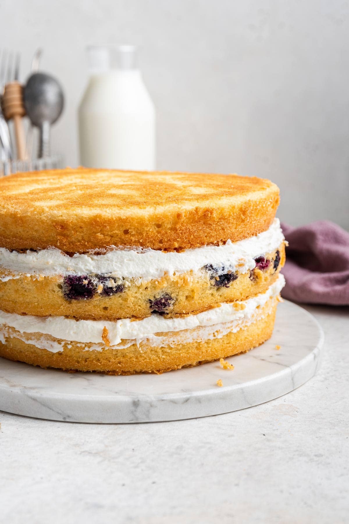 three layers of blueberry cake with layers of blueberry curd before a crumb coat