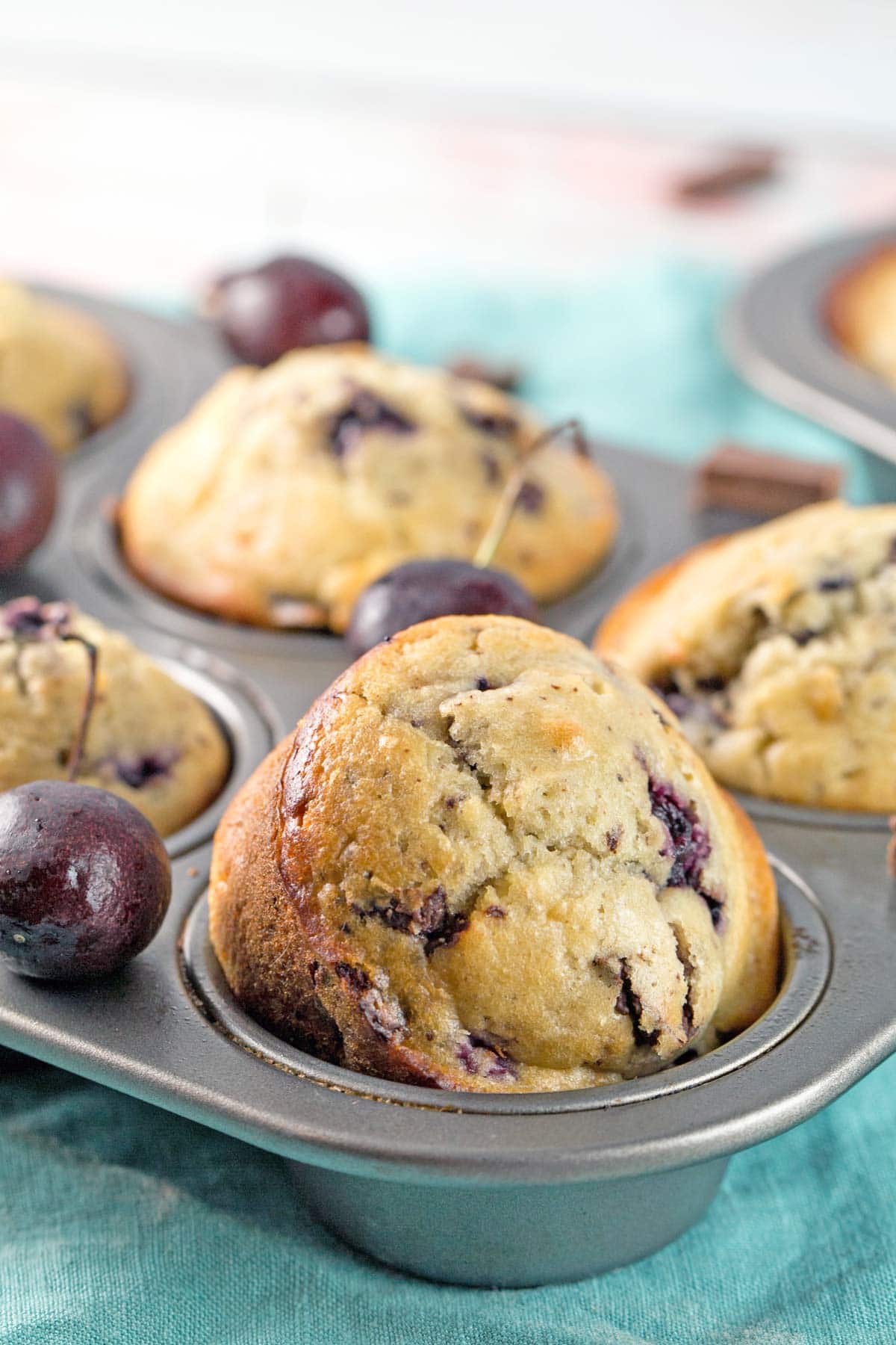 cherry chocolate chunk muffins in a muffin tin with one muffin partially removed and tiled towards the camera