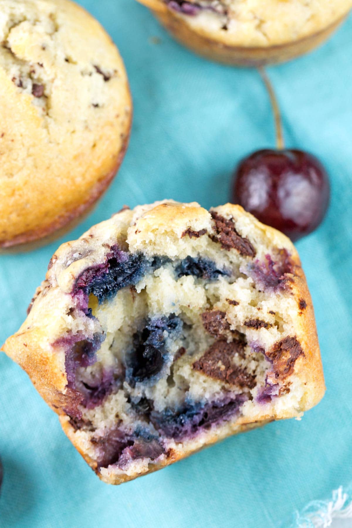 a cherry chocolate chunk muffin cut in half showing the inside with the purple and blue hue of fresh cherries in baked goods