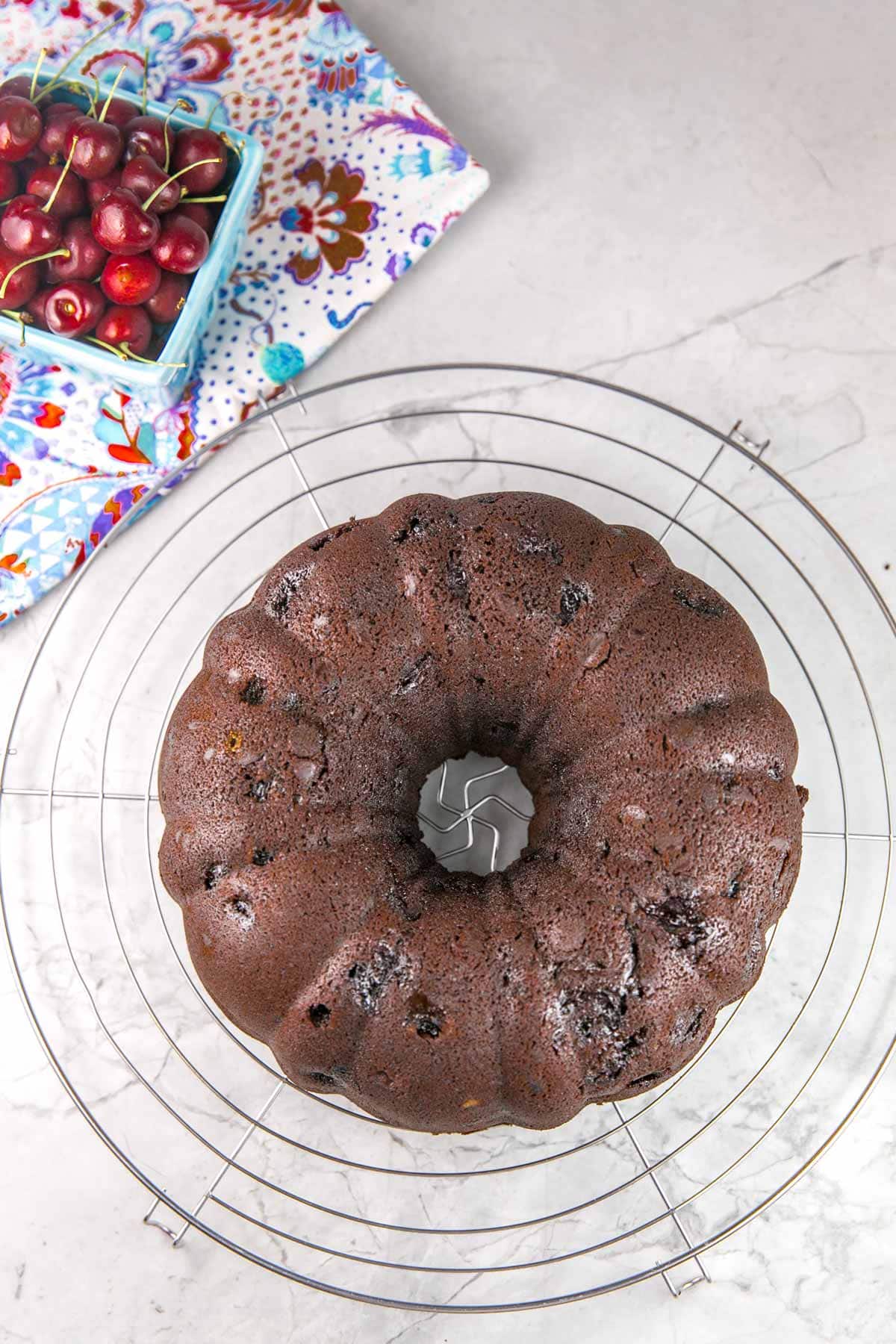 overhead view of a bundt cake on a round cooling rack with fresh cherries in the background