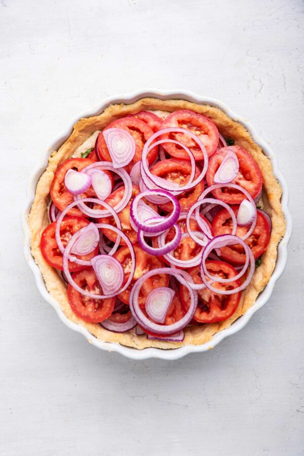 unbaked tomato pie in a pie crust with layers of tomatoes, red onion, and basil