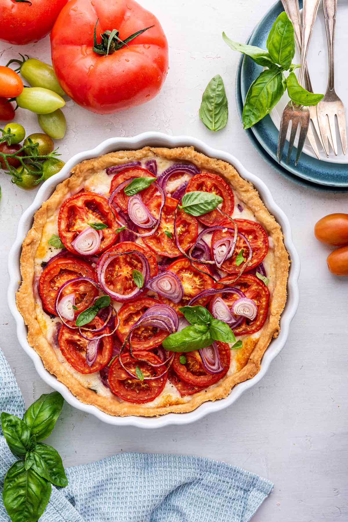 tomato pie in a white ceramic pie plate next to fresh tomatoes and basil