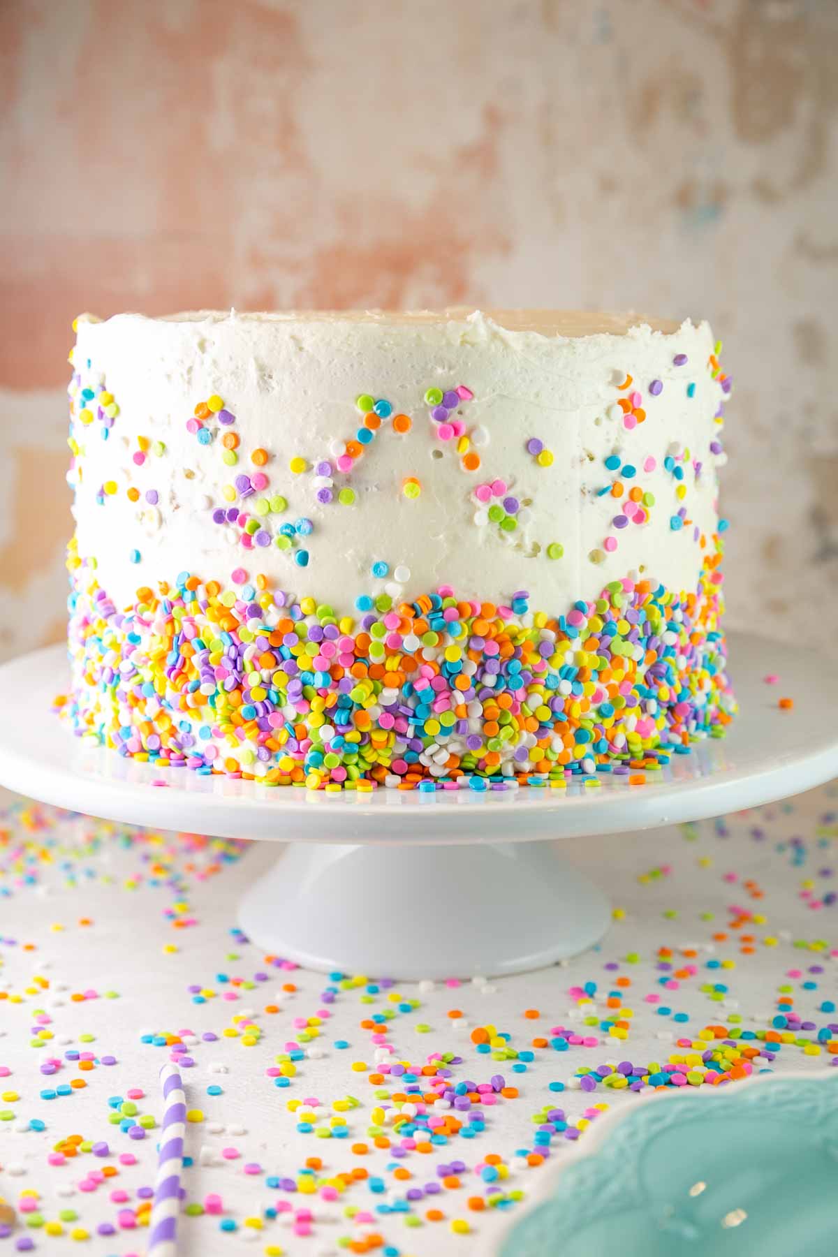 three layer funfetti cake covered with white frosting and pastel candy quins
