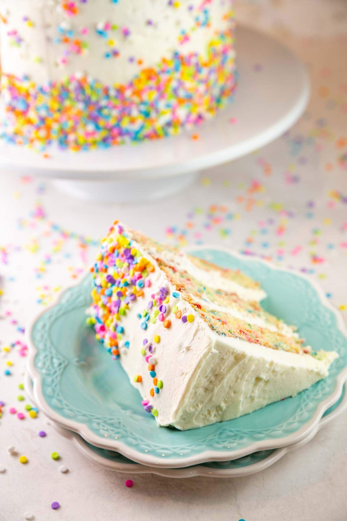 slice of funfetti cake on a stack of dessert plates surrounded by pastel sprinkles
