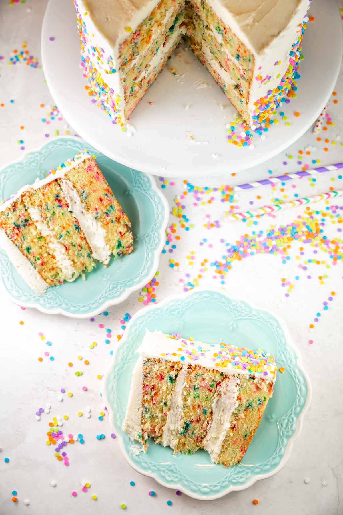 overhead view of three layer cakes on blue dessert plates with colorful paper straws