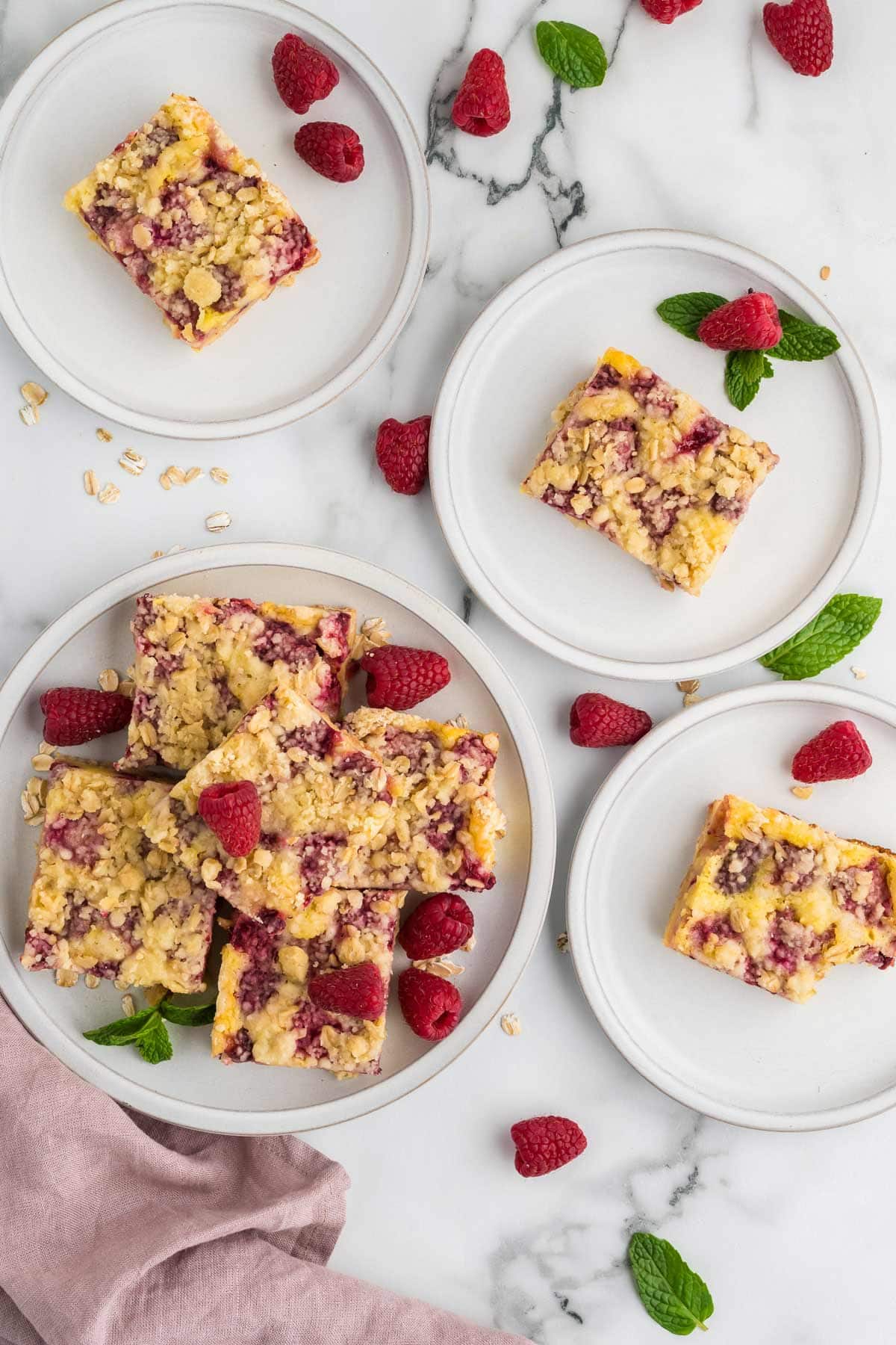 One plate with lots of raspberry pie bars next to three plates each with one bar on them. 