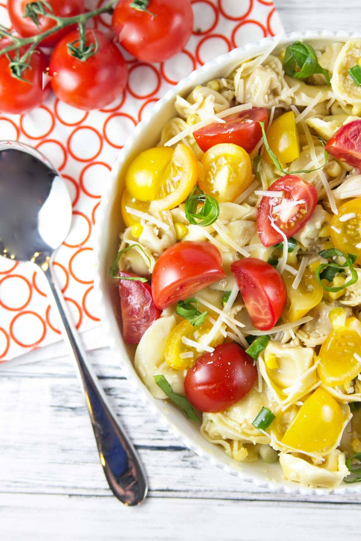 a bowl of tomato basil tortellini salad full of fresh yellow and red tomatoes