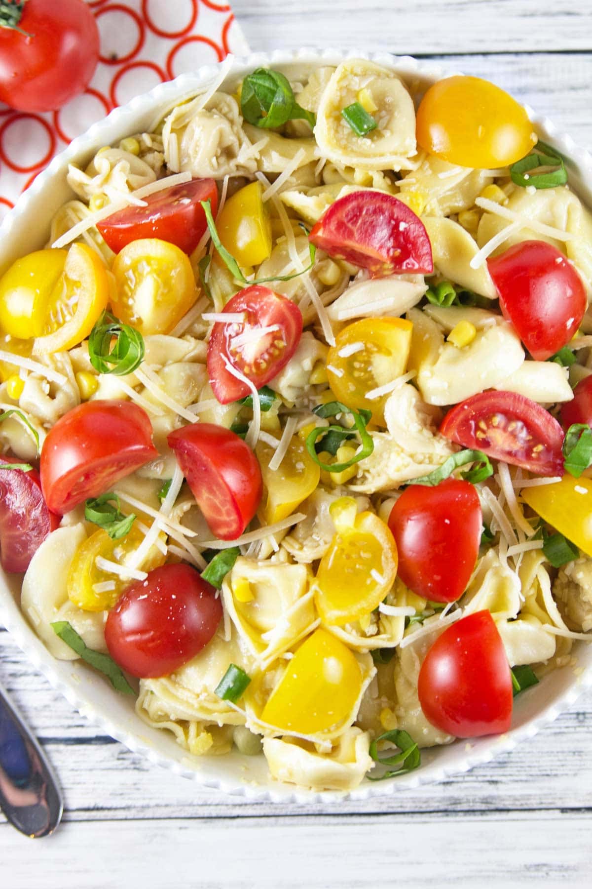 overhead view of a large white bowl filled with tortellini, fresh summer tomatoes, and basil