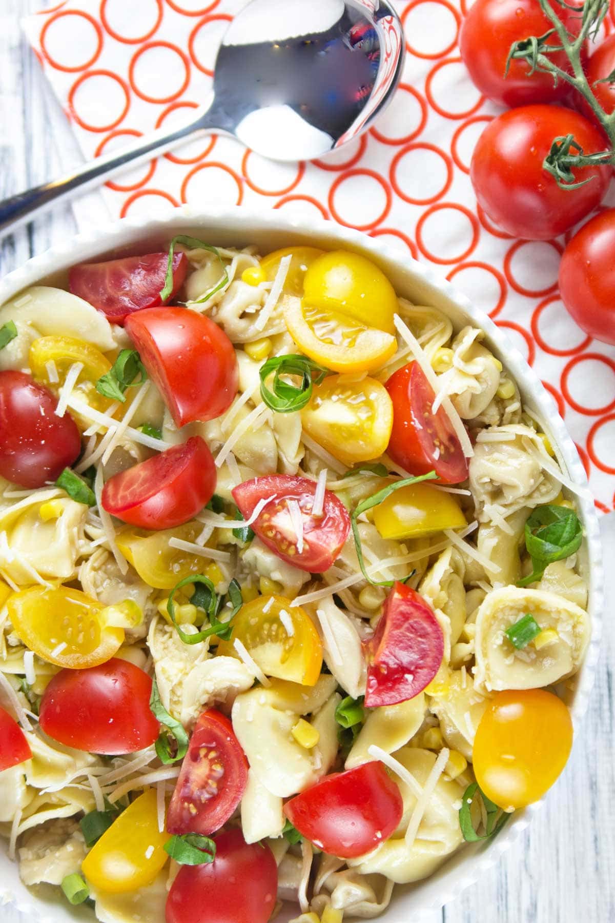 tomato basil tortellini salad on a red and white dish towel with fresh red grape tomatoes still on the vine