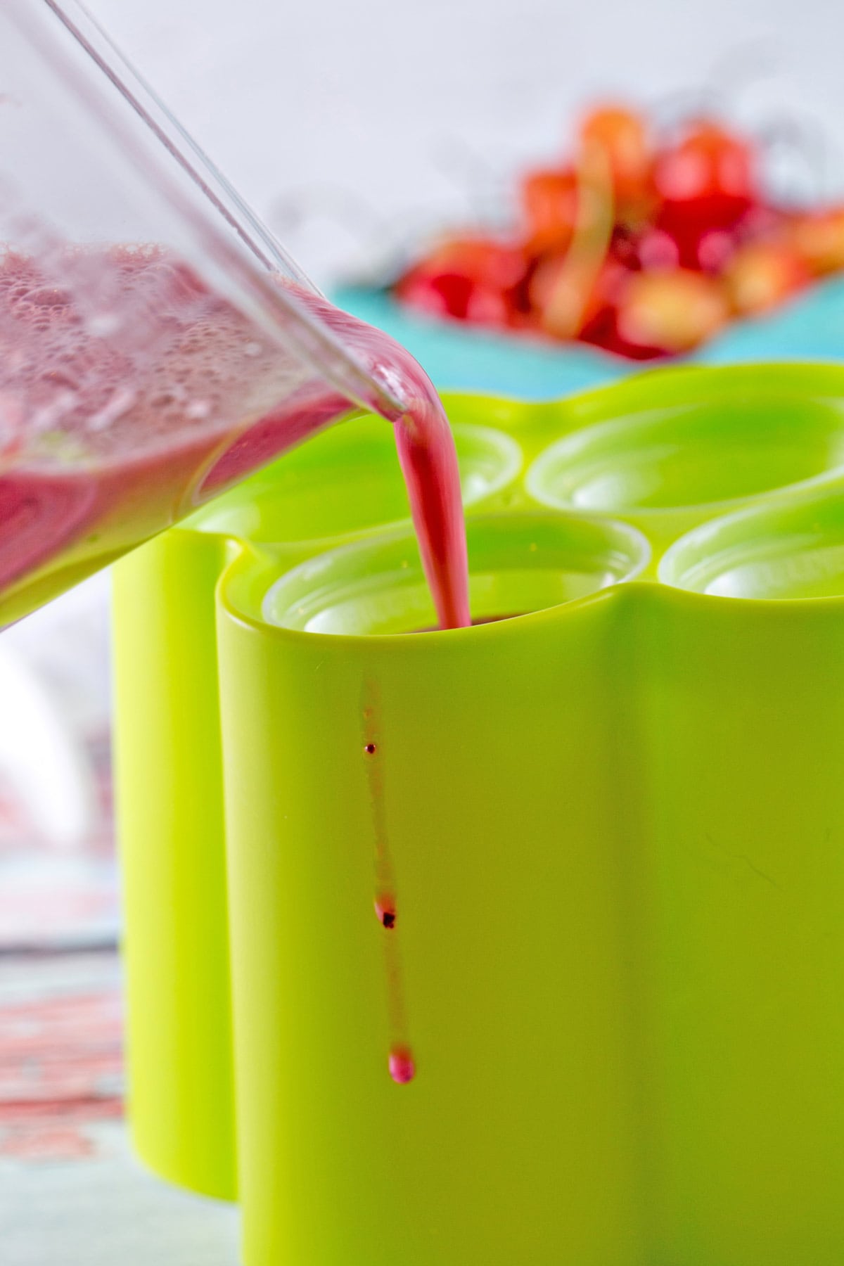 pouring a watermelon and cherry puree mixture into green popsicle molds
