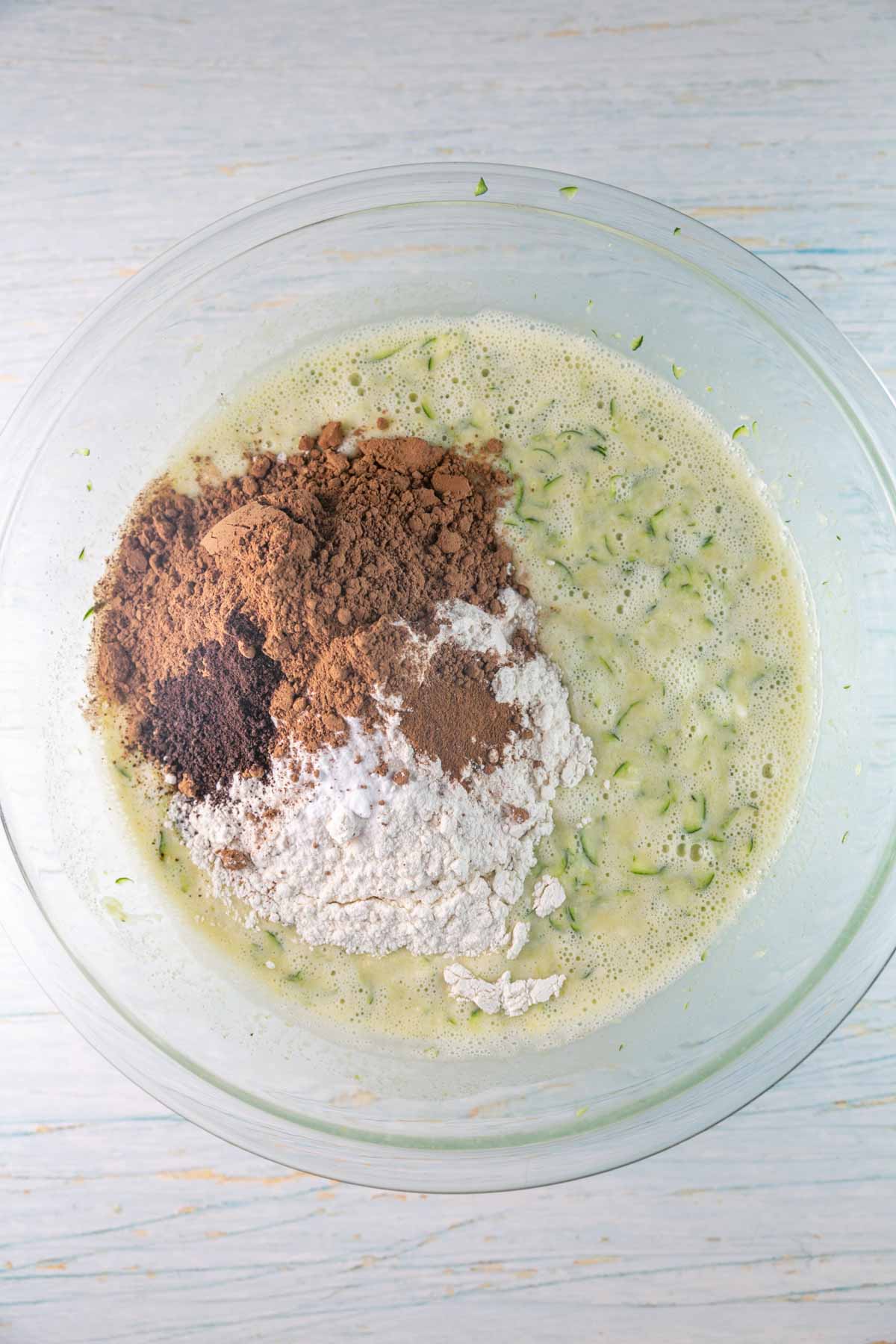 adding the ingredients to make a chocolate zucchini cake into a glass mixing bowl