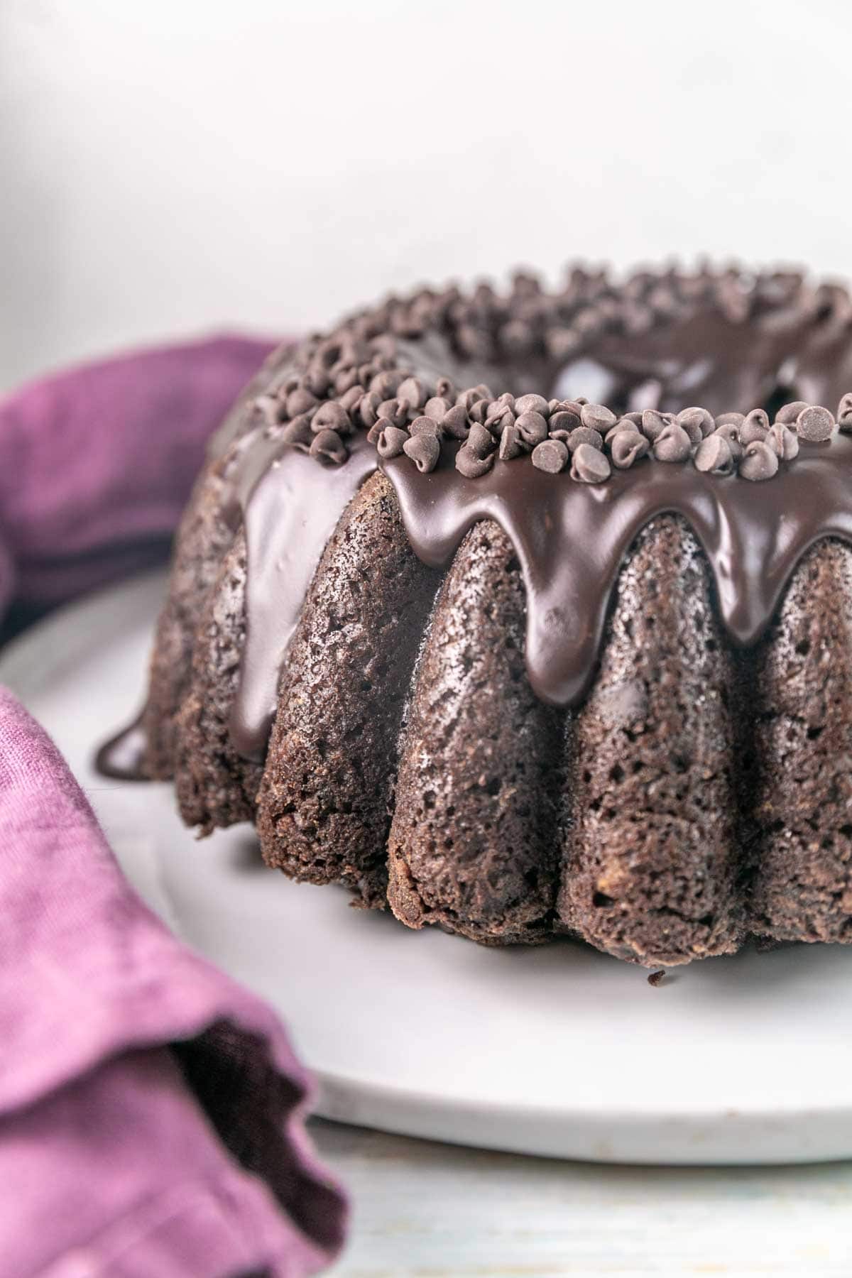 Zucchini chocolate bundt cake on a serving platter topped with ganache and chocolate chips. 